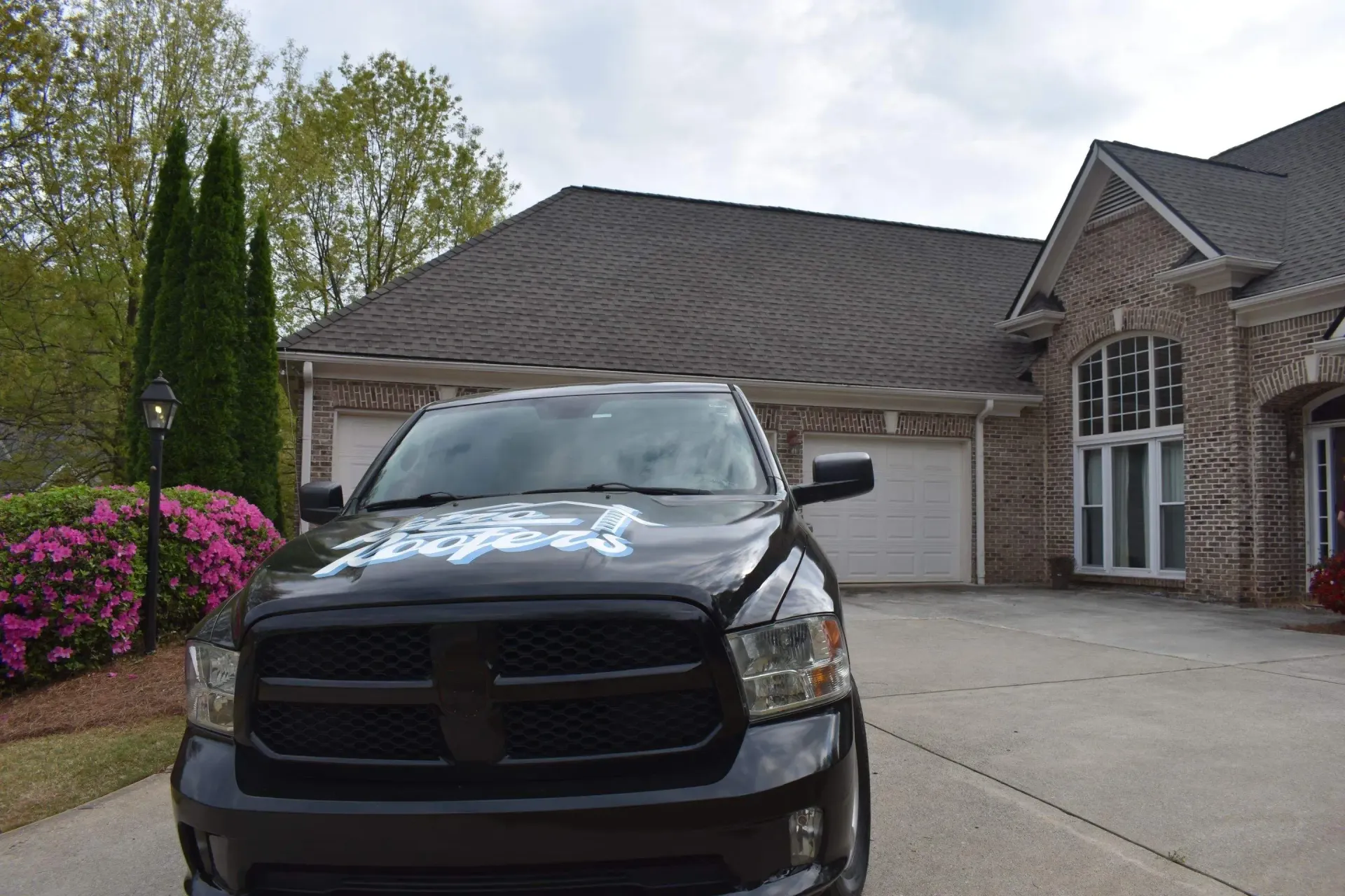 Black truck parked in front of a brick house with a three-car garage on a cloudy day.