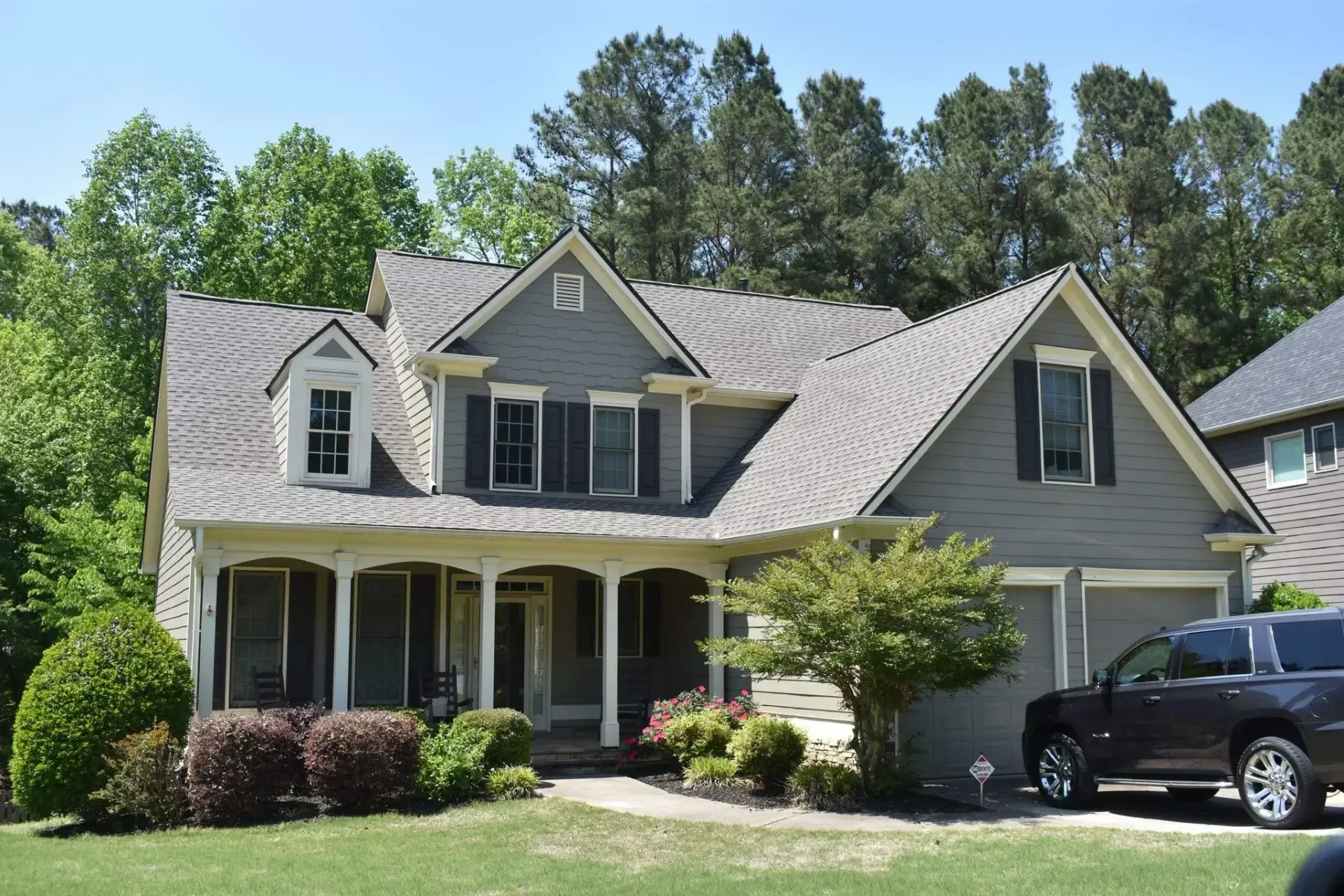 Gray house with a porch and attached garage, black SUV parked in the driveway.