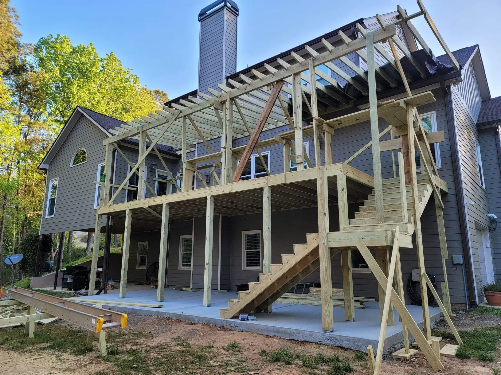 New wooden deck construction attached to a two-story house. The framework is mostly complete.