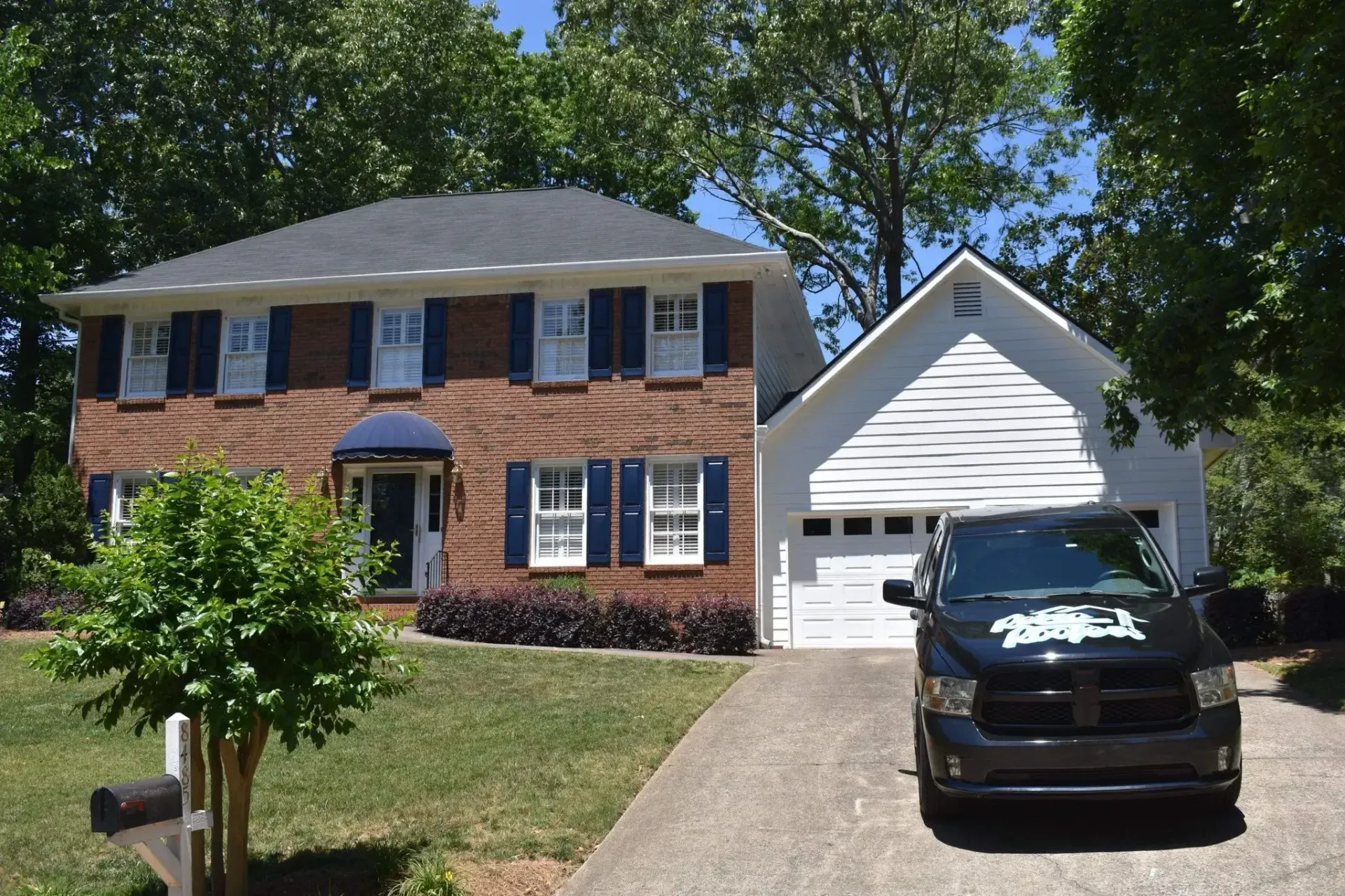 Two-story brick house with blue shutters and a driveway with a black truck parked in front.
