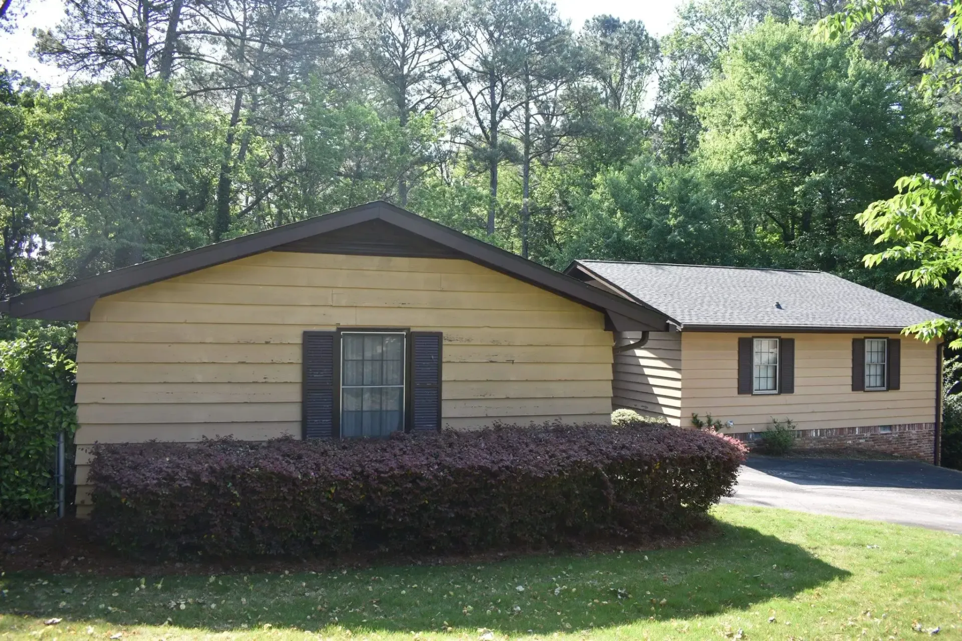 Brown cabin with black shutters and a dark roof, surrounded by greenery and trees.