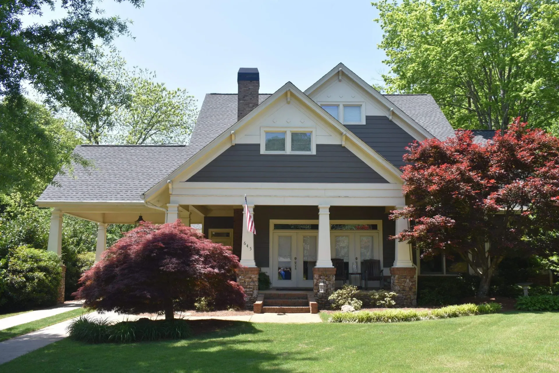 Curb-side view of a Craftsman-style house with a covered porch, gray siding, and a manicured lawn.
