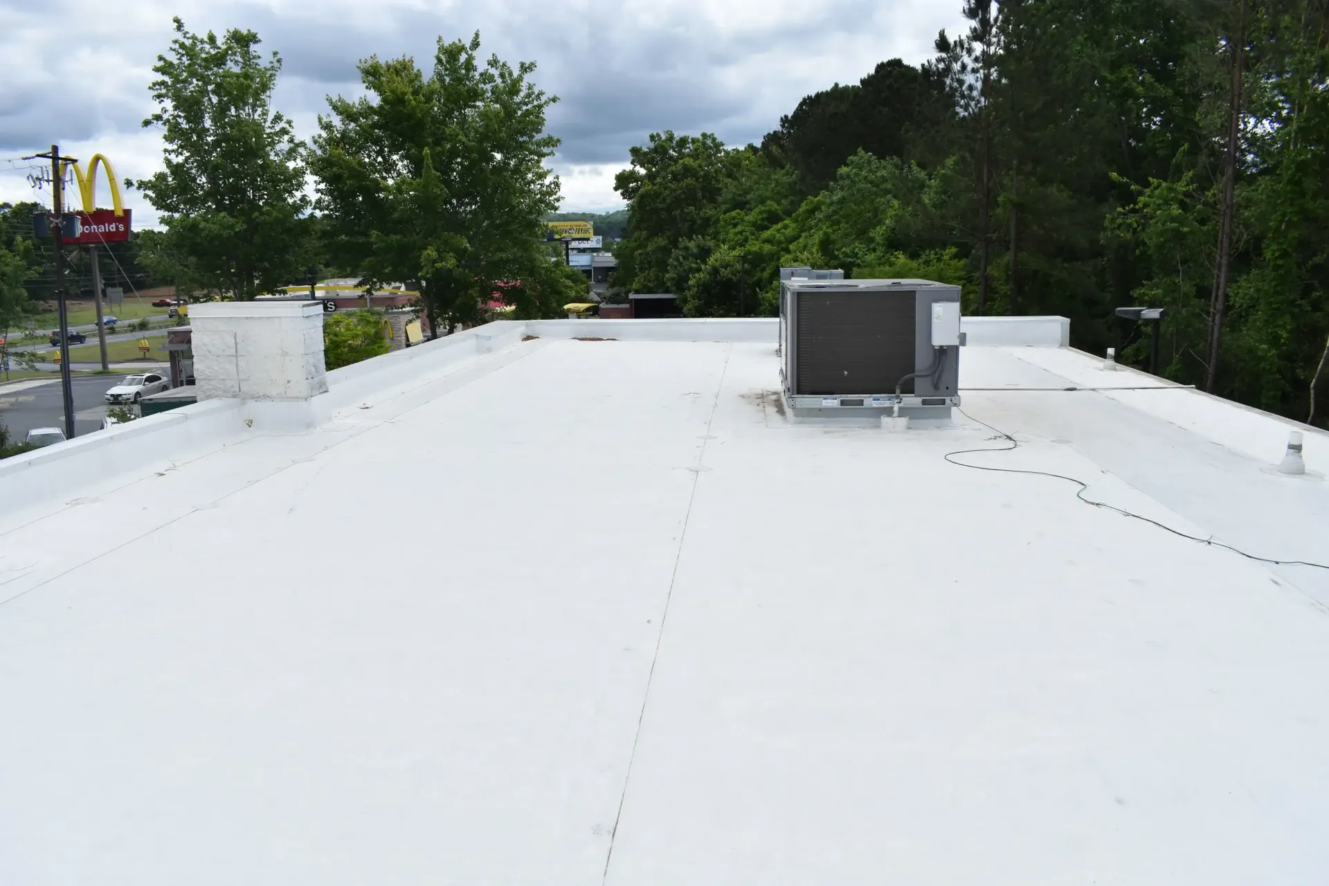 White flat roof with HVAC unit and chimney against a cloudy sky, trees, and a McDonald's sign.