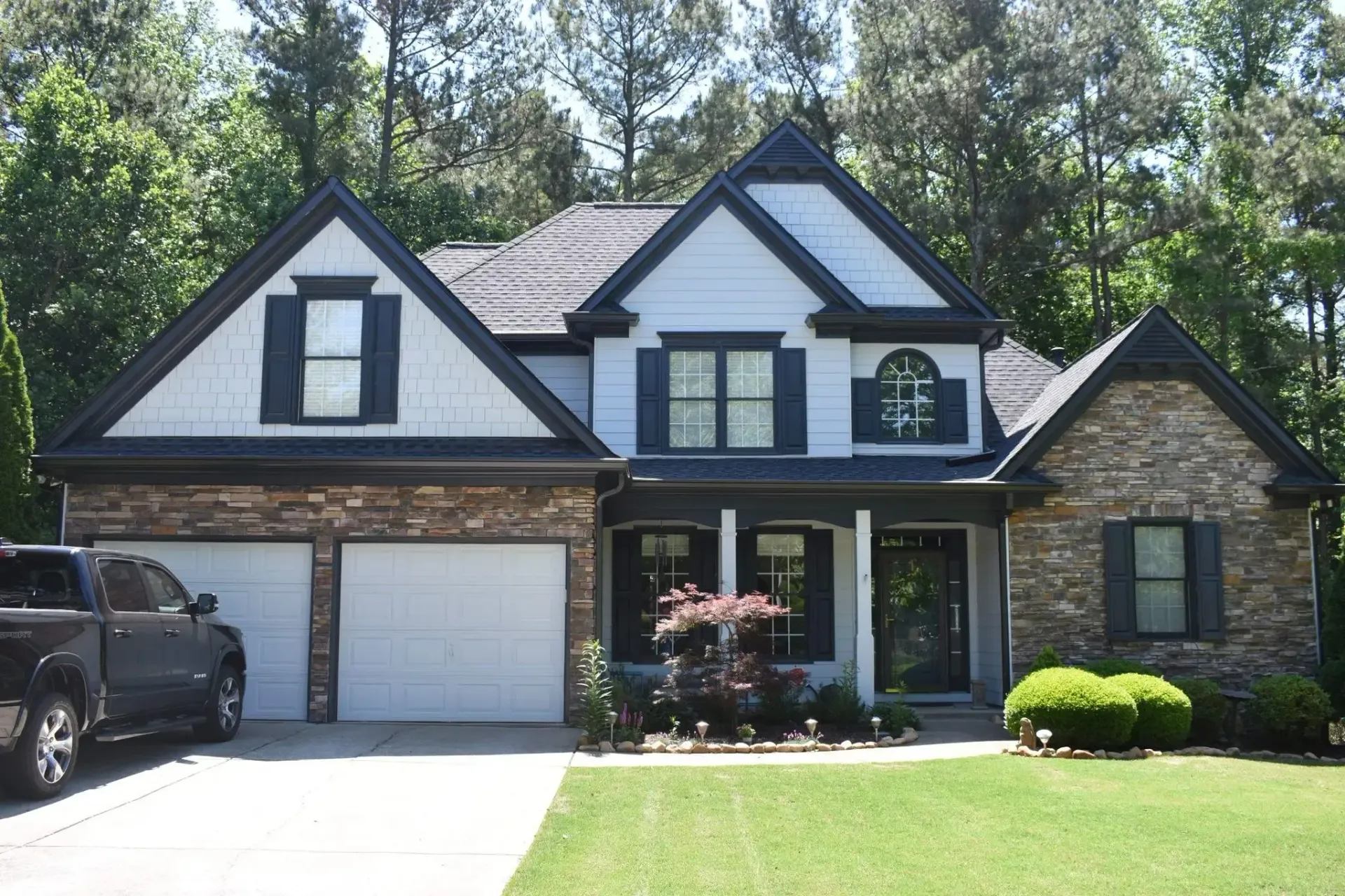Two-story house with light blue siding, stone accents, black shutters, and a green lawn. A black truck is parked in the driveway.