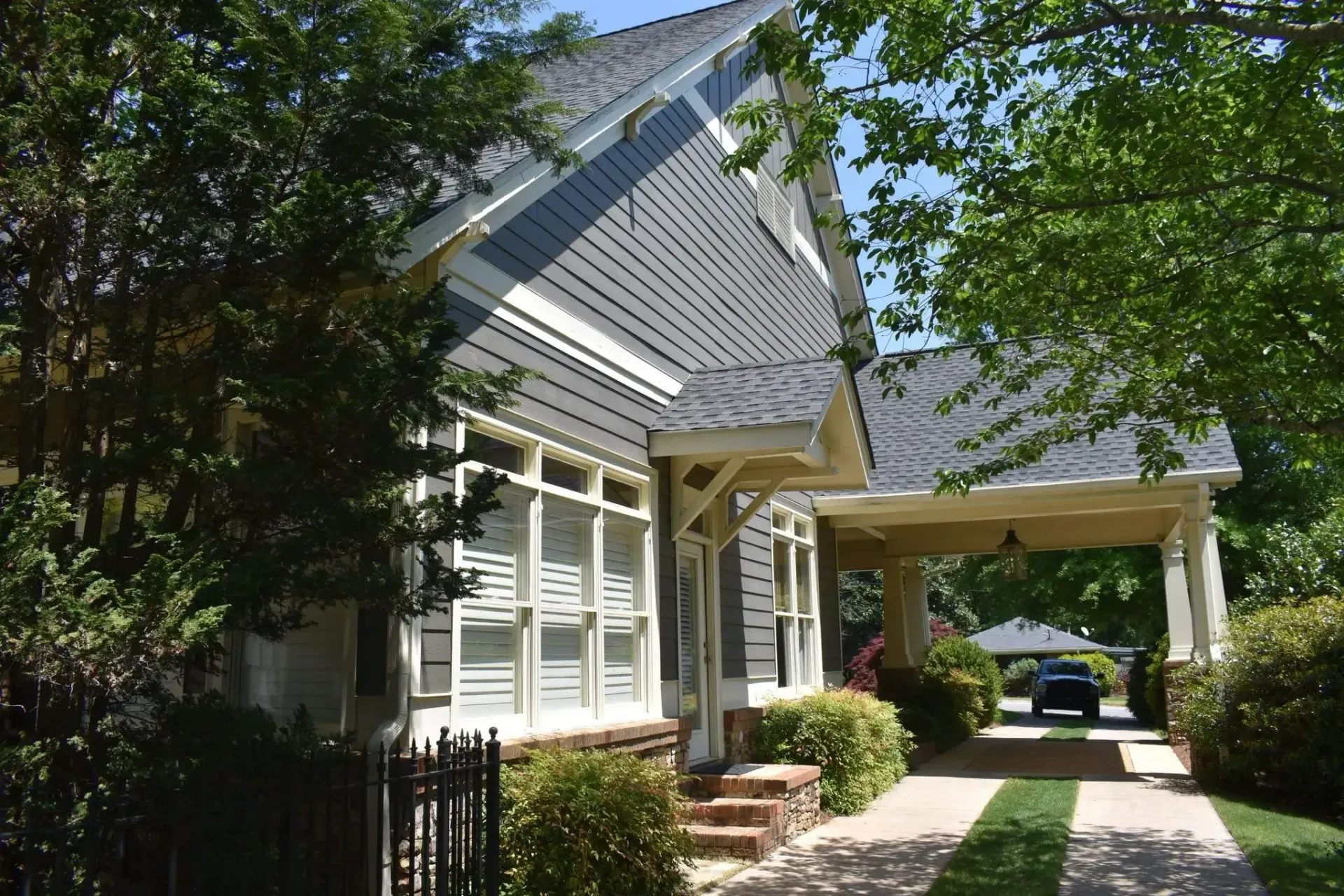 Gray and white Craftsman-style house with a carport, driveway, and greenery.