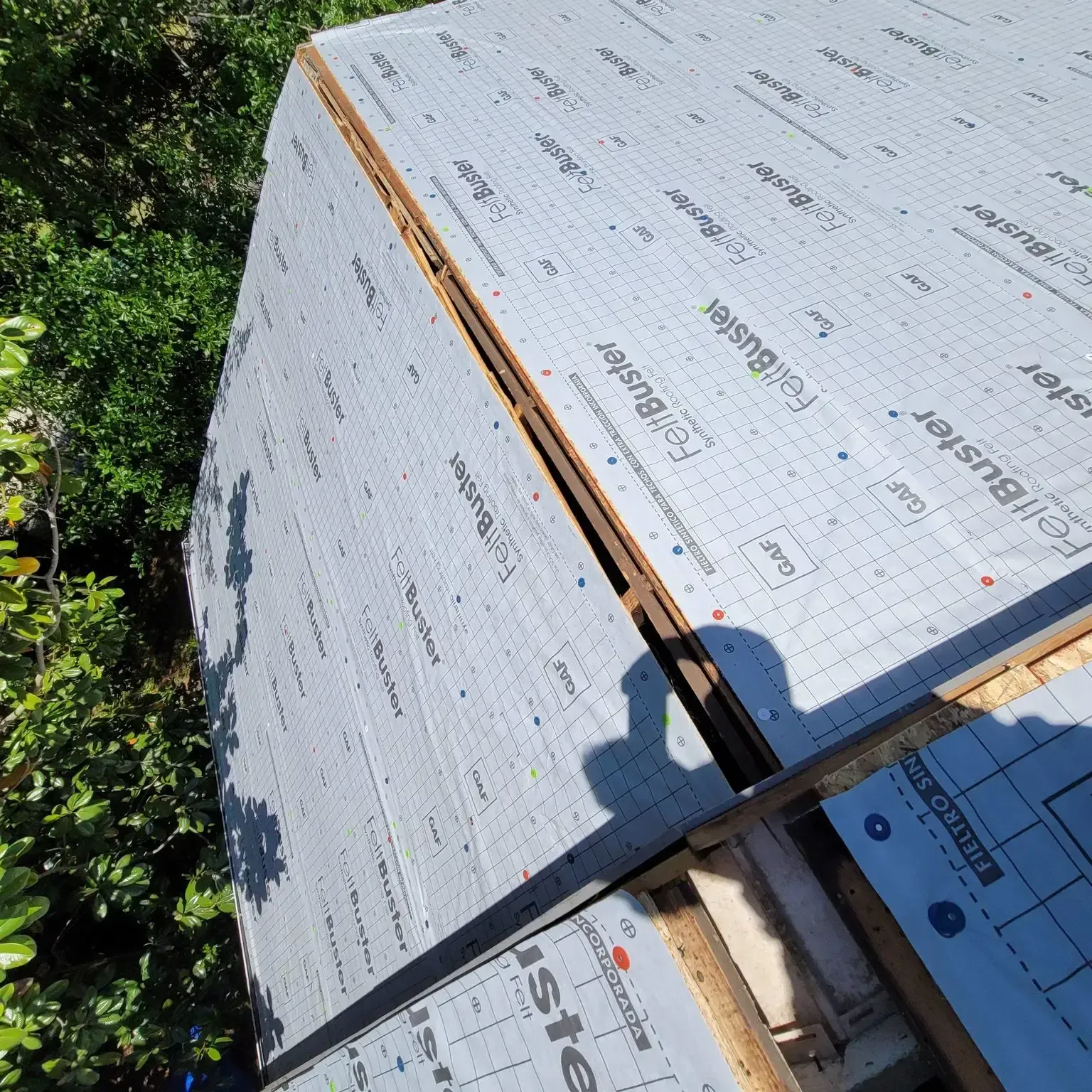 Roof under construction, covered in grey underlayment. Sunlight, trees in background.