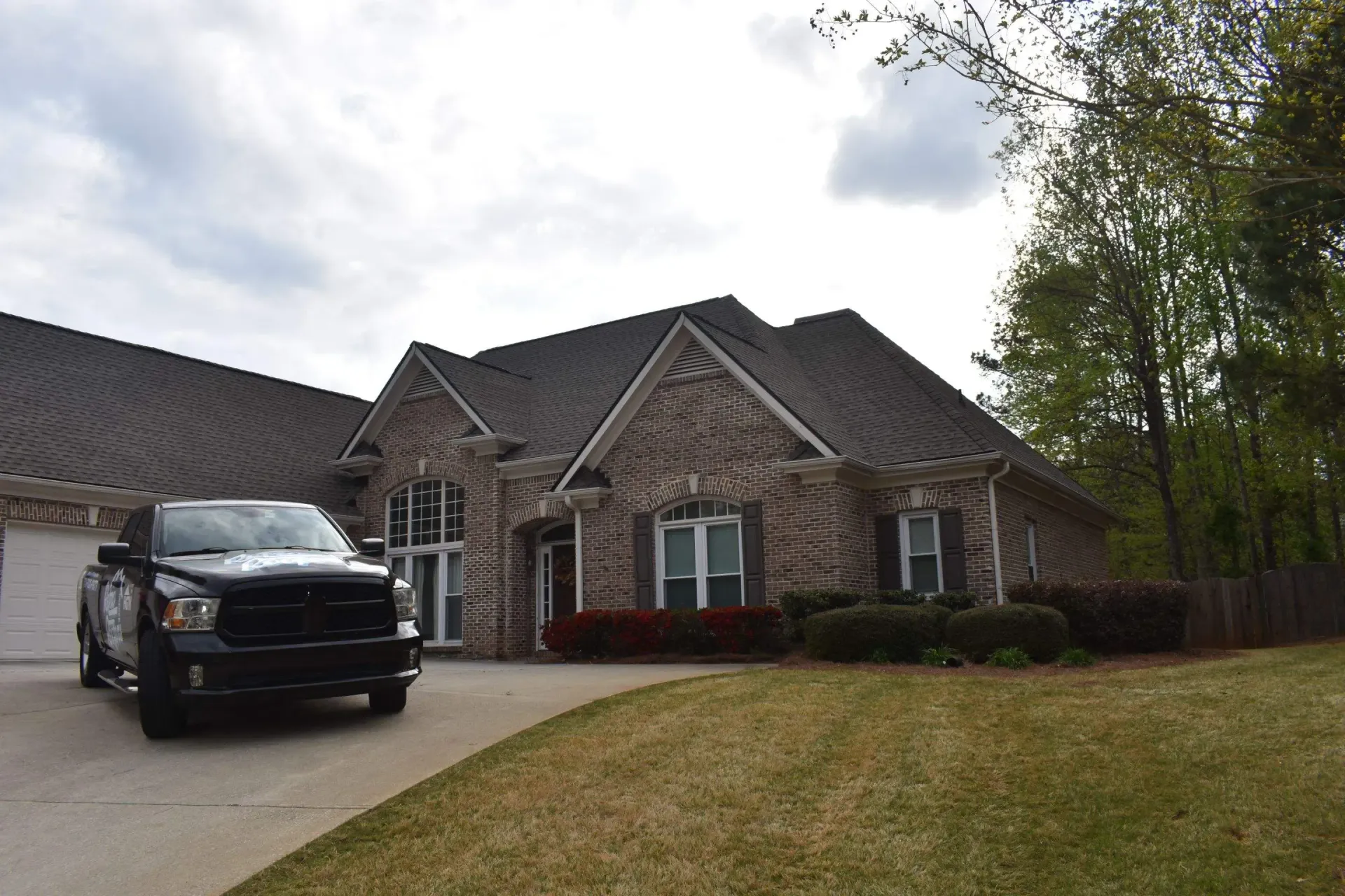 Black truck parked in front of a brick house with a dark roof and a green lawn.