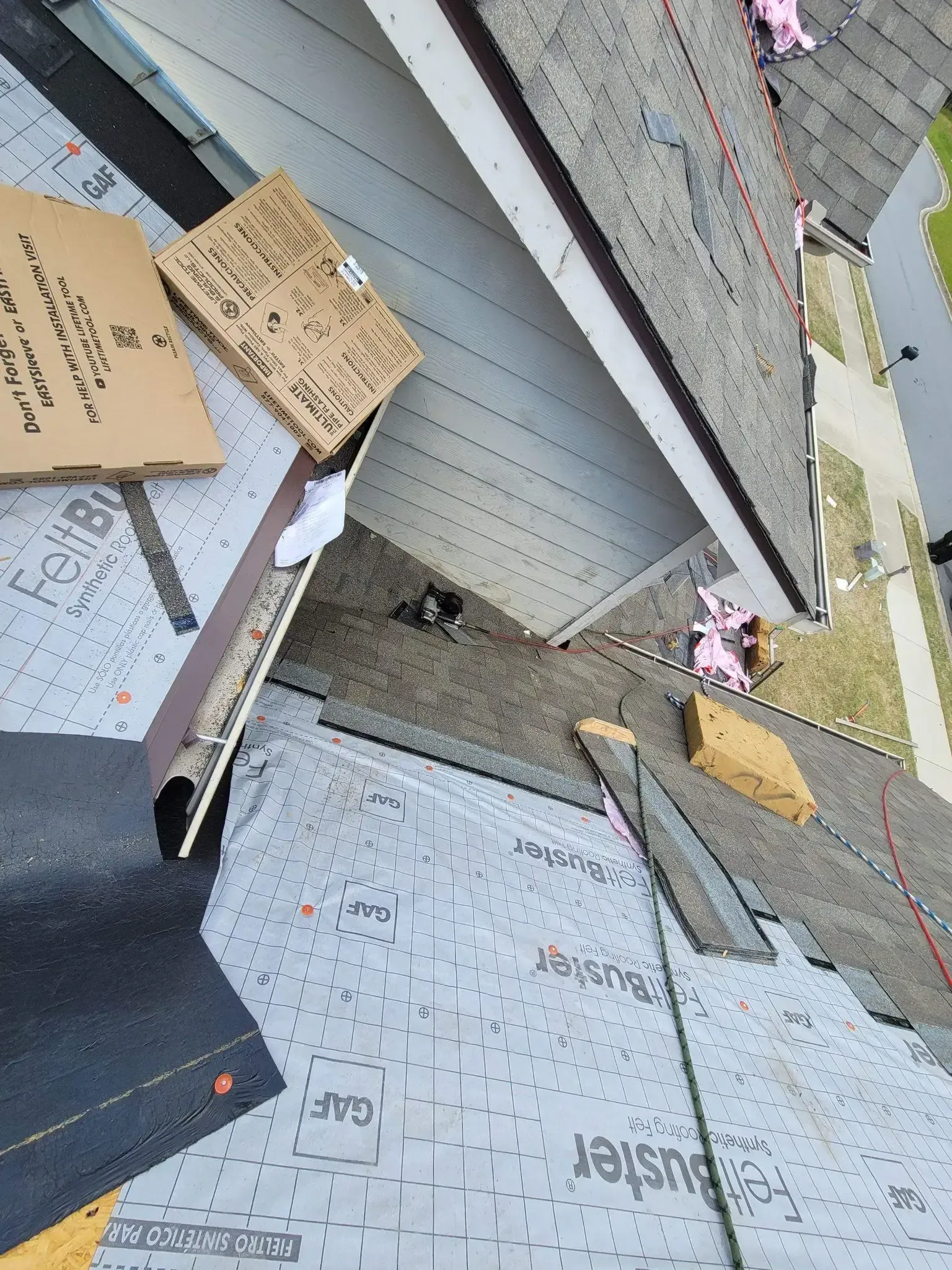 Rooftop with shingles, flashing, and underlayment. Cardboard boxes and building materials scattered.