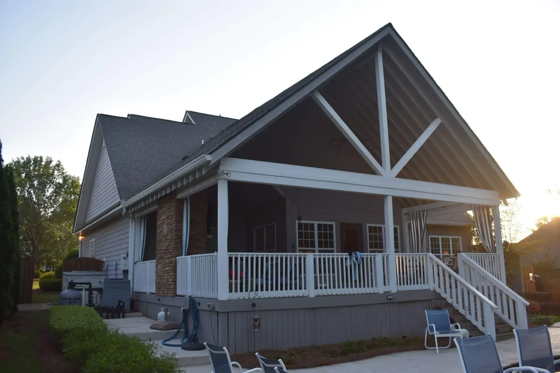 House with a porch and a pool area. Gray roof and siding, white railings, and blue chairs are visible.