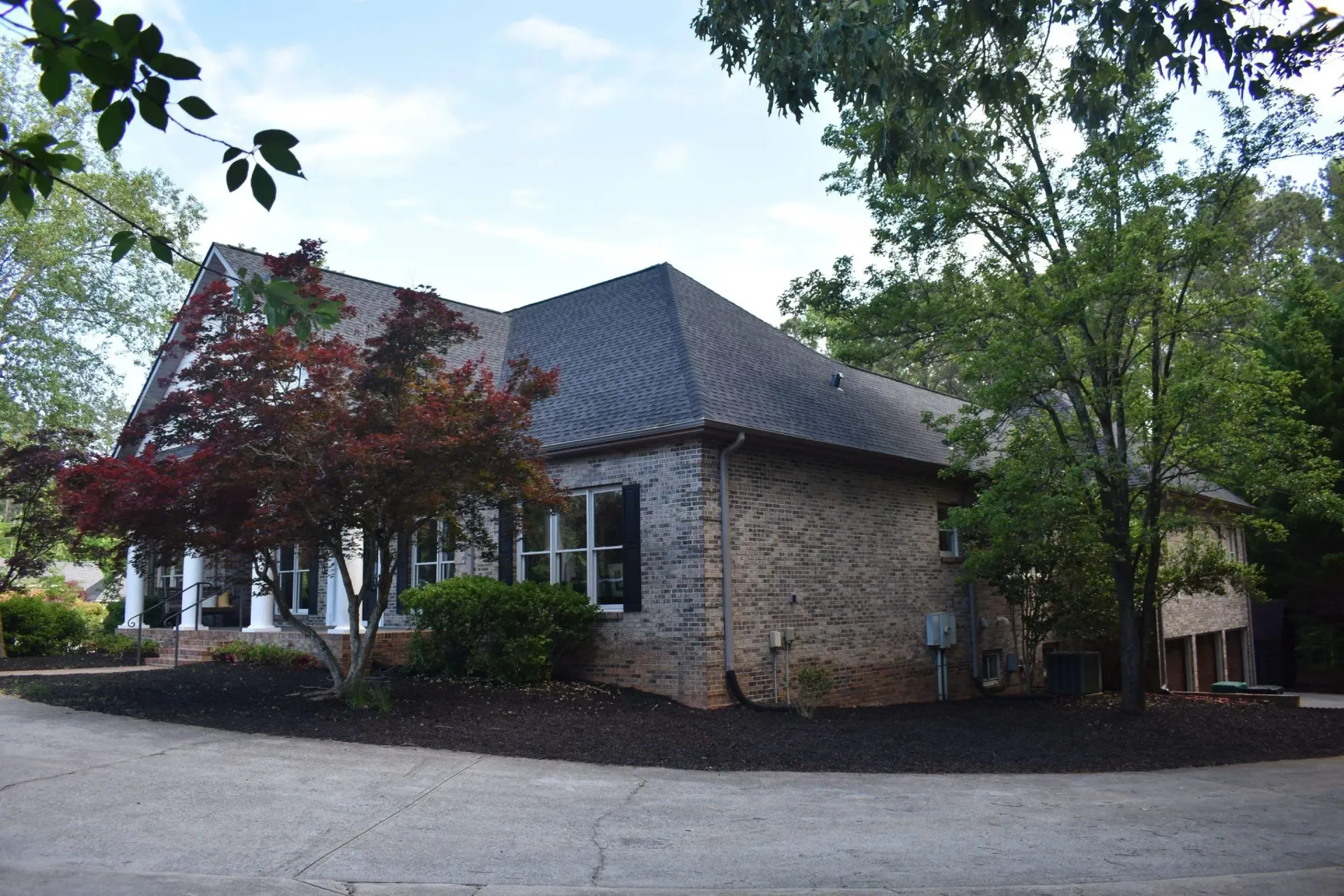 Brick building with dark roof, black shutters, and manicured landscaping; trees frame the structure.