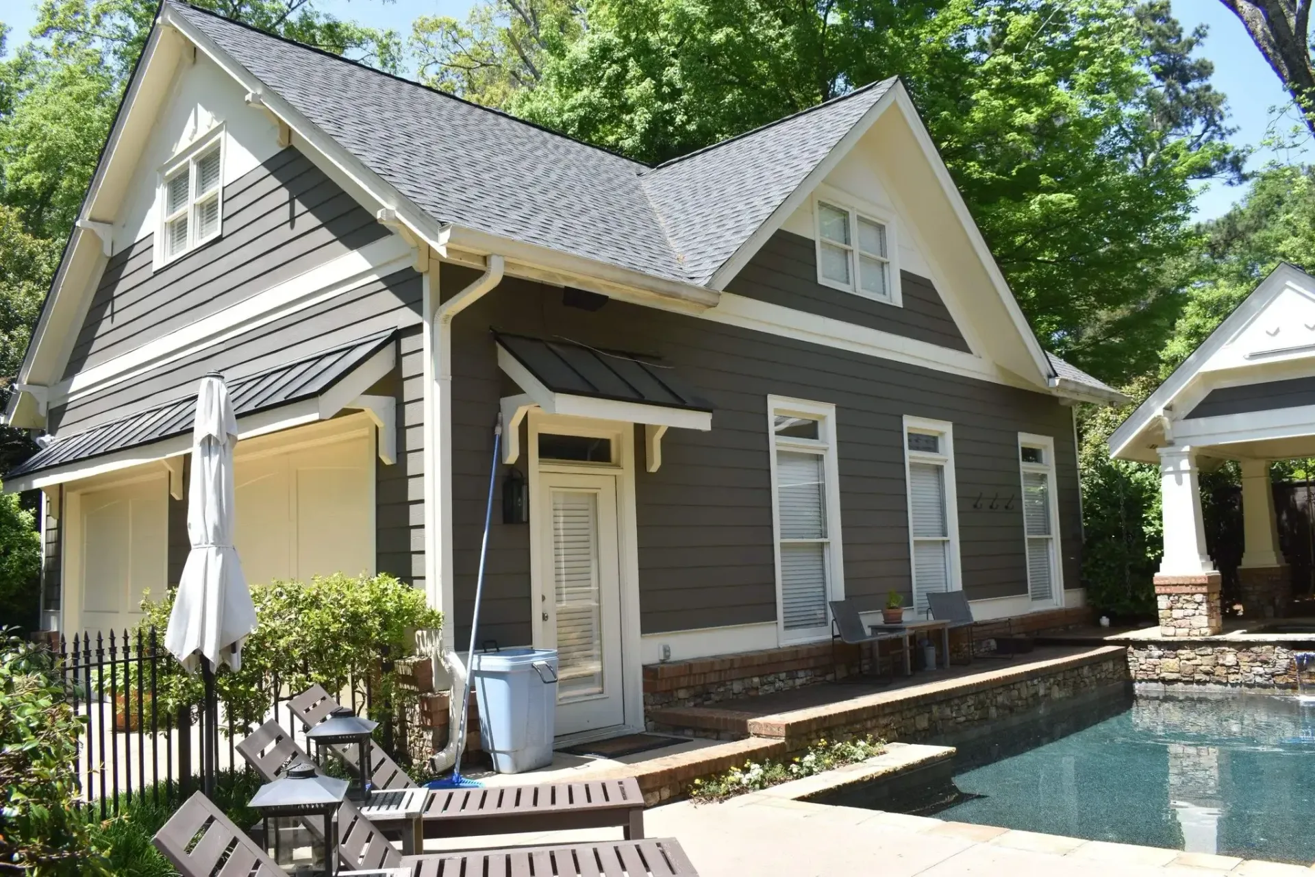 Gray and white building with a pool, trees in the background; outdoor seating visible.