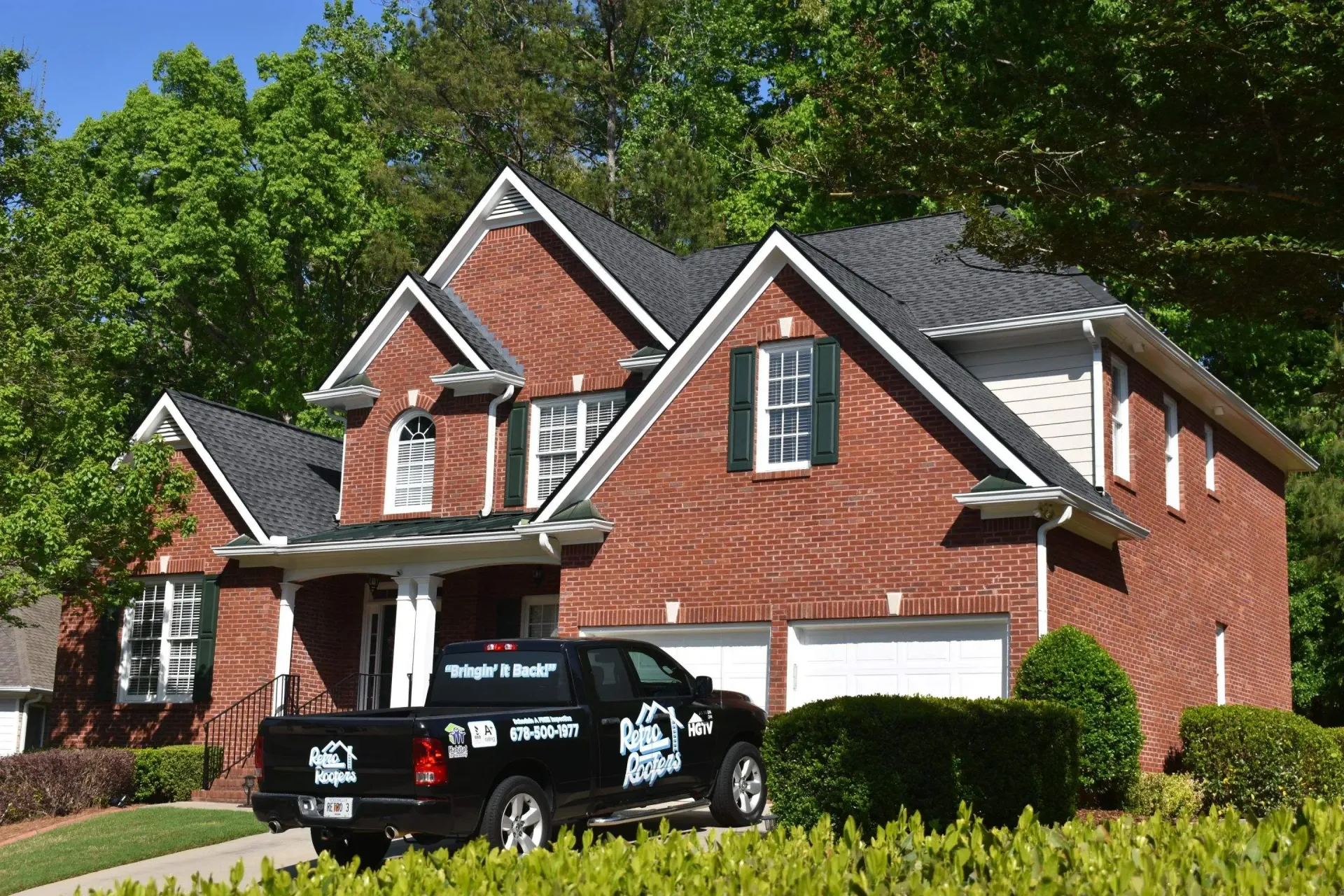 Brick house with black roof, green shutters, and black pickup truck parked in front.