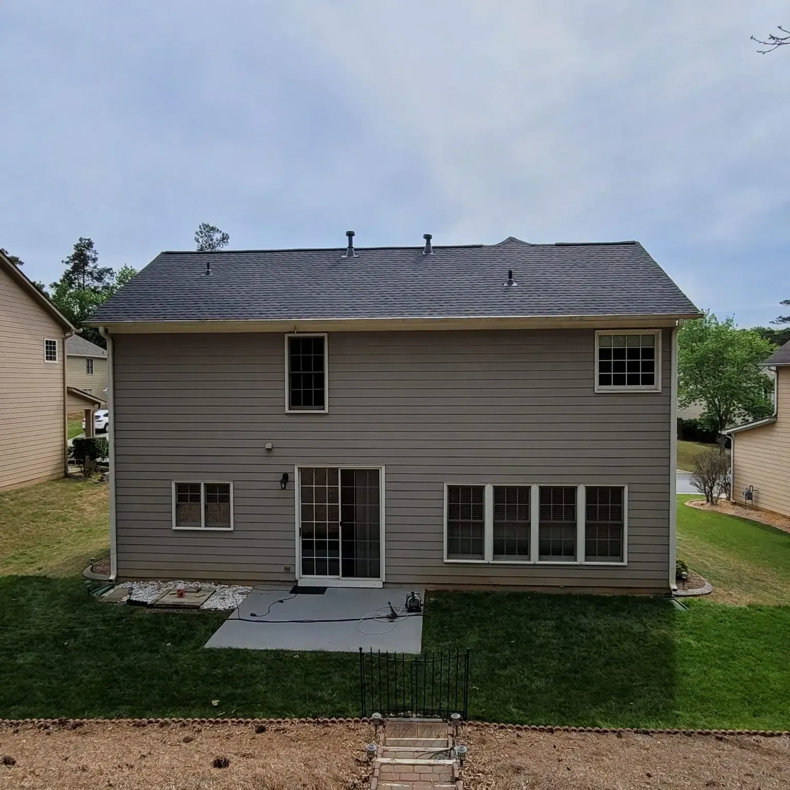 Back of a two-story beige house with dark roof. Sliding glass door and multiple windows. Green lawn.
