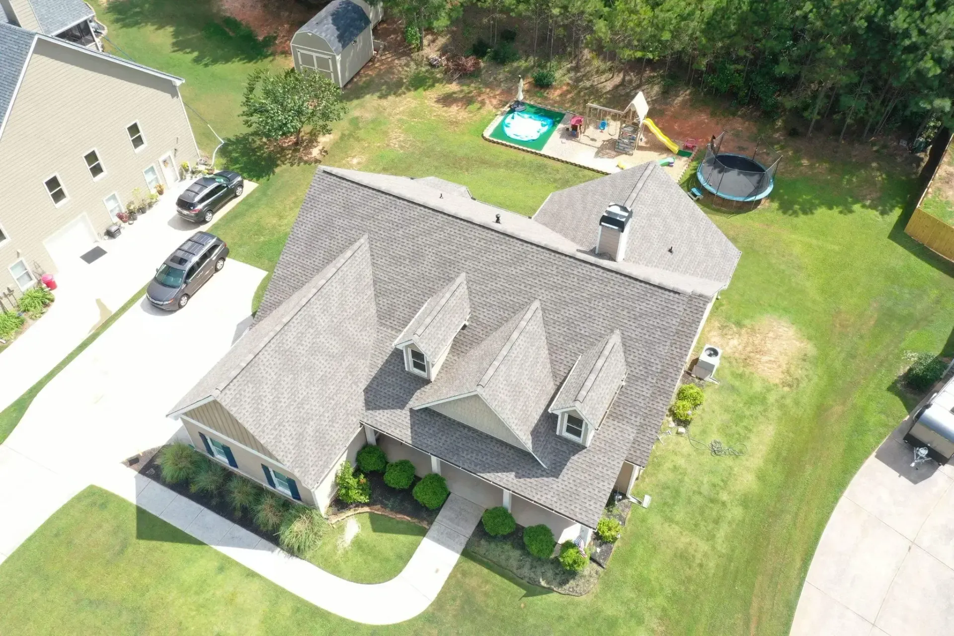 Aerial view of a house with a brown roof, green lawn, and a driveway with parked cars.