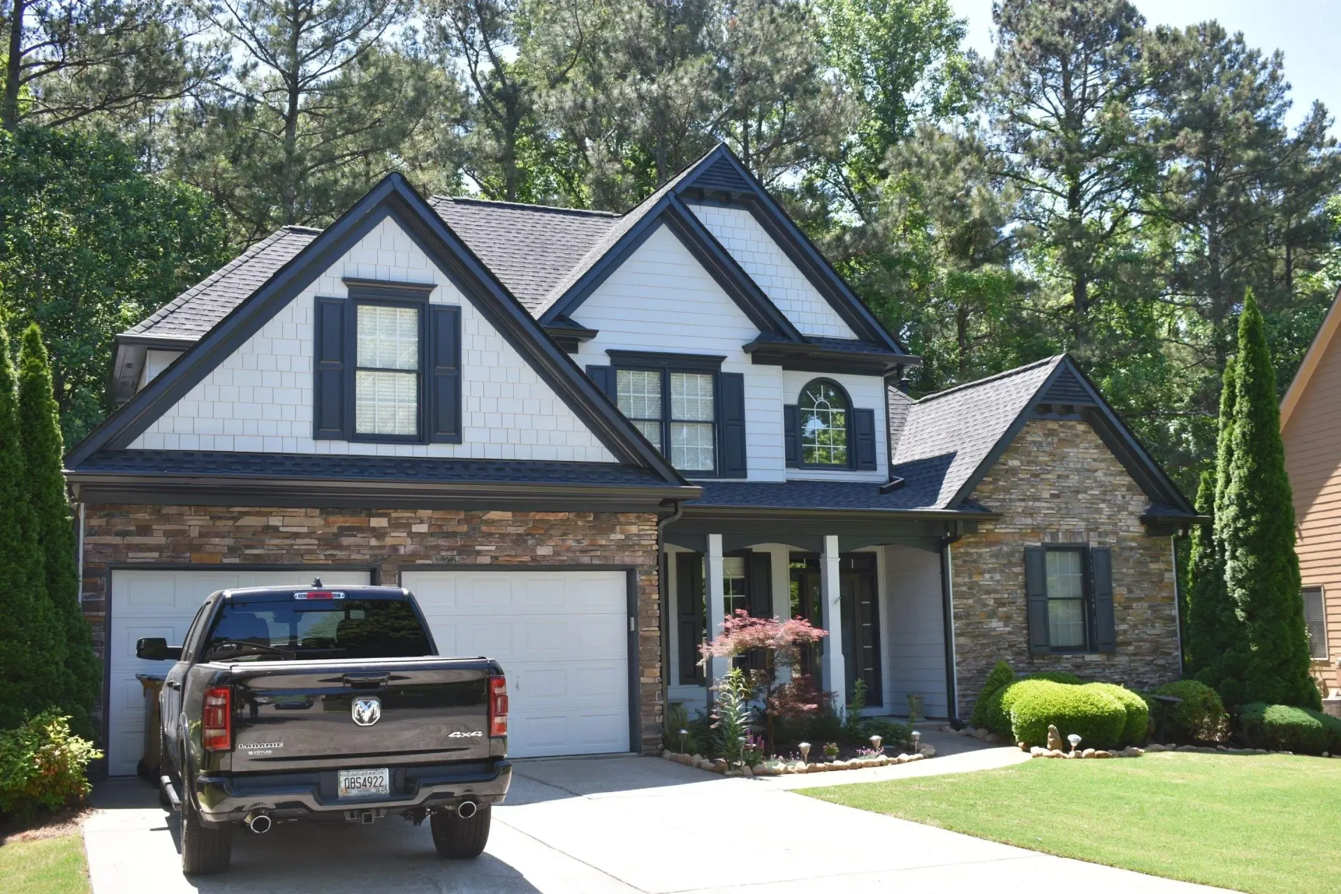 Two-story house with stone and gray siding, blue shutters, and a black pickup truck in the driveway.
