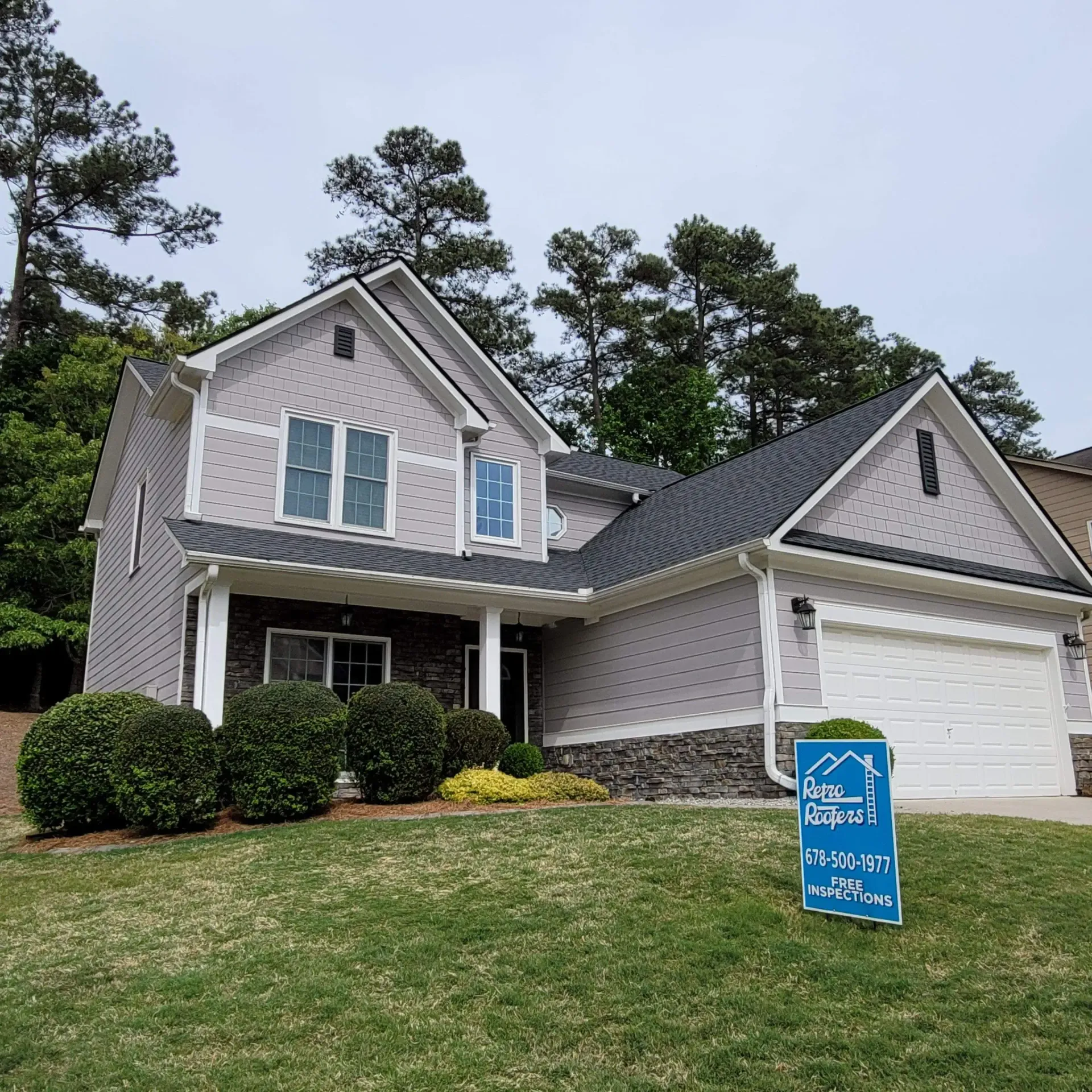 House with gray siding and stone accents, a white garage door, and a blue sign on the lawn.