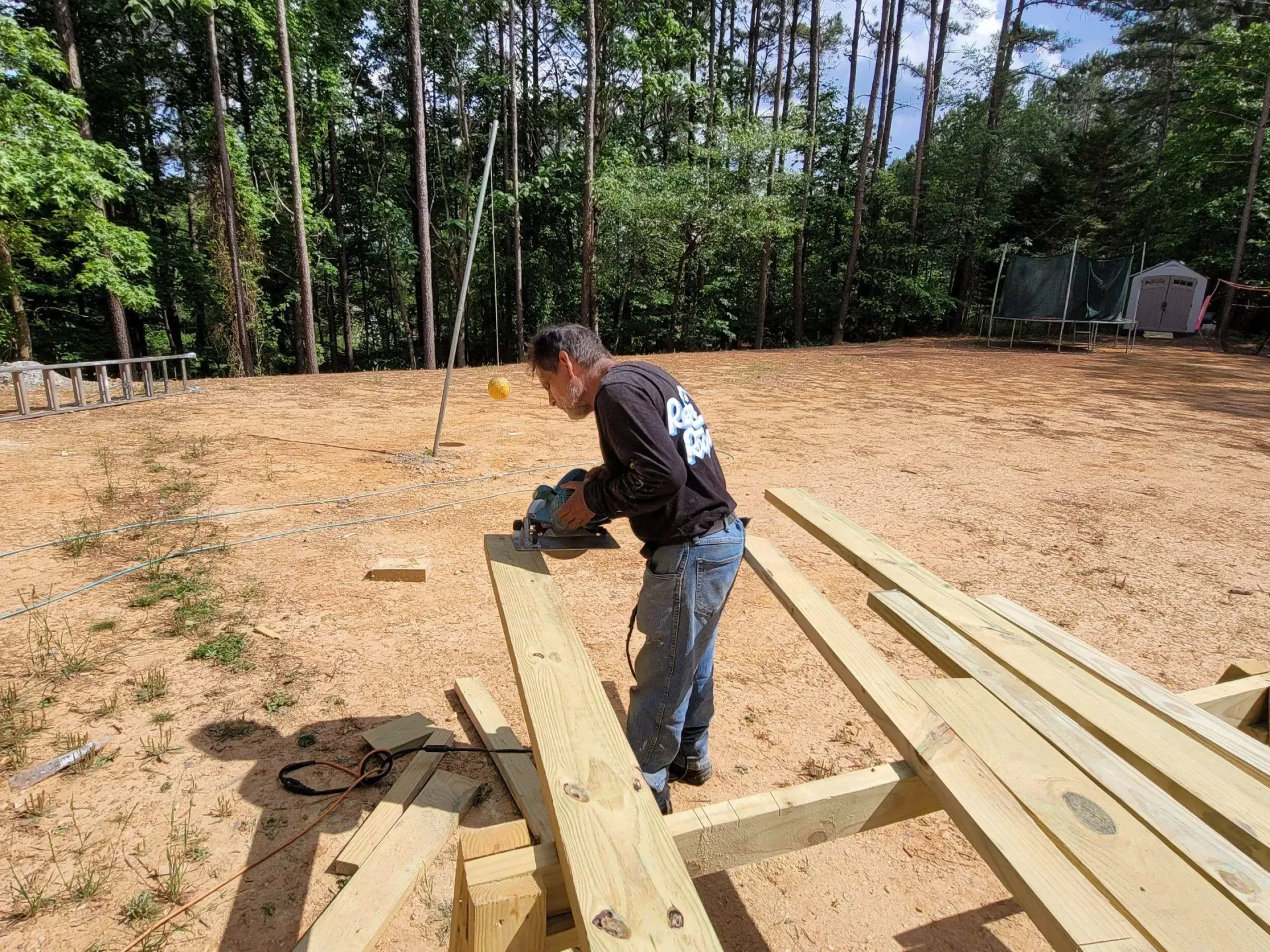 Man using a circular saw on wooden planks outdoors; a construction project in progress.