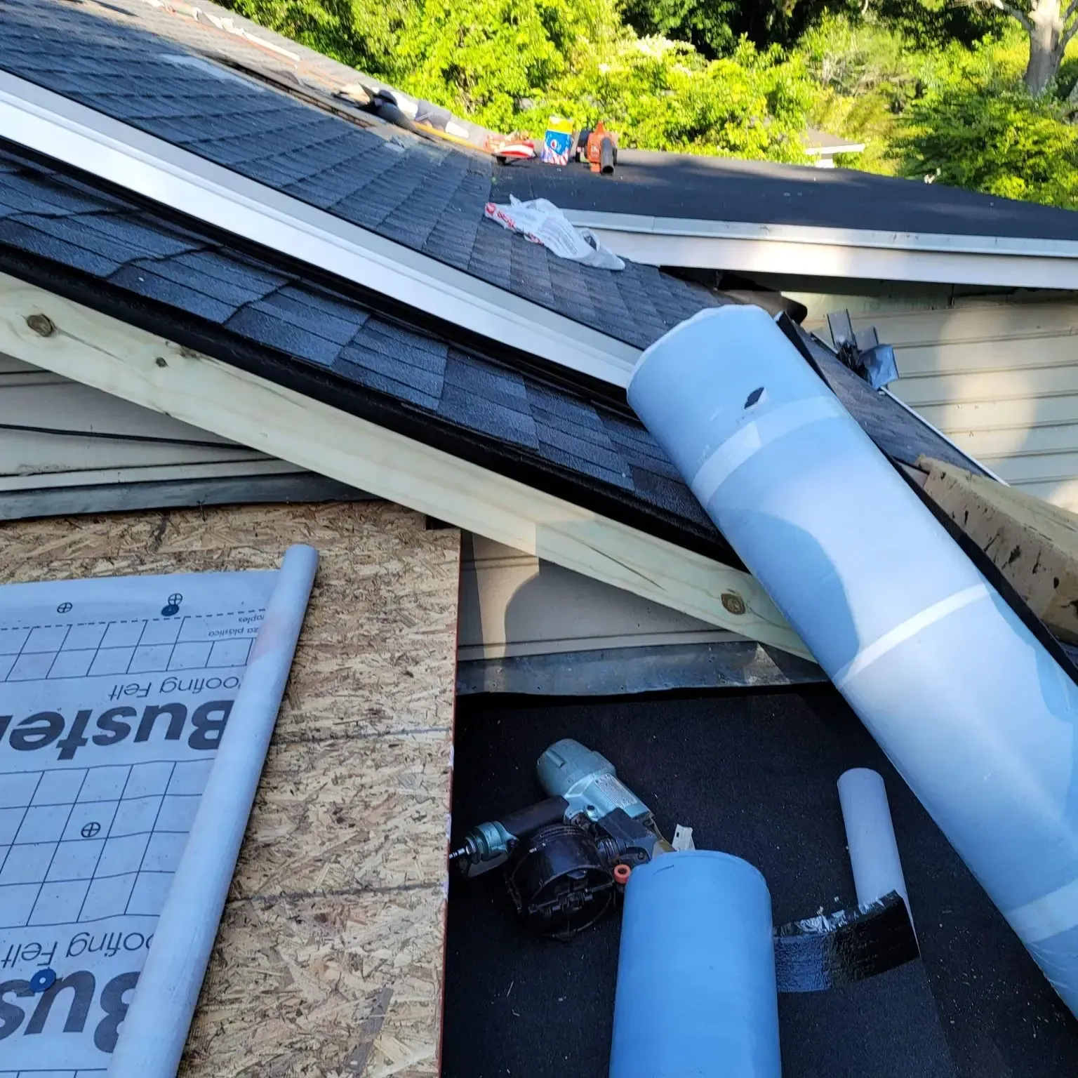 Roofing work in progress: a roll of blue underlayment, tools, and partially shingled roof.