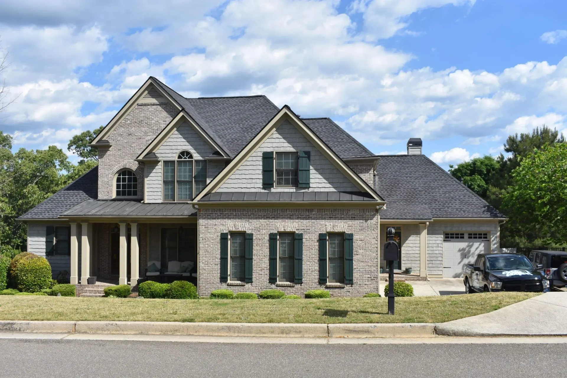 Brick house with gray roof, shutters, and a two-car garage, parked car in the driveway.