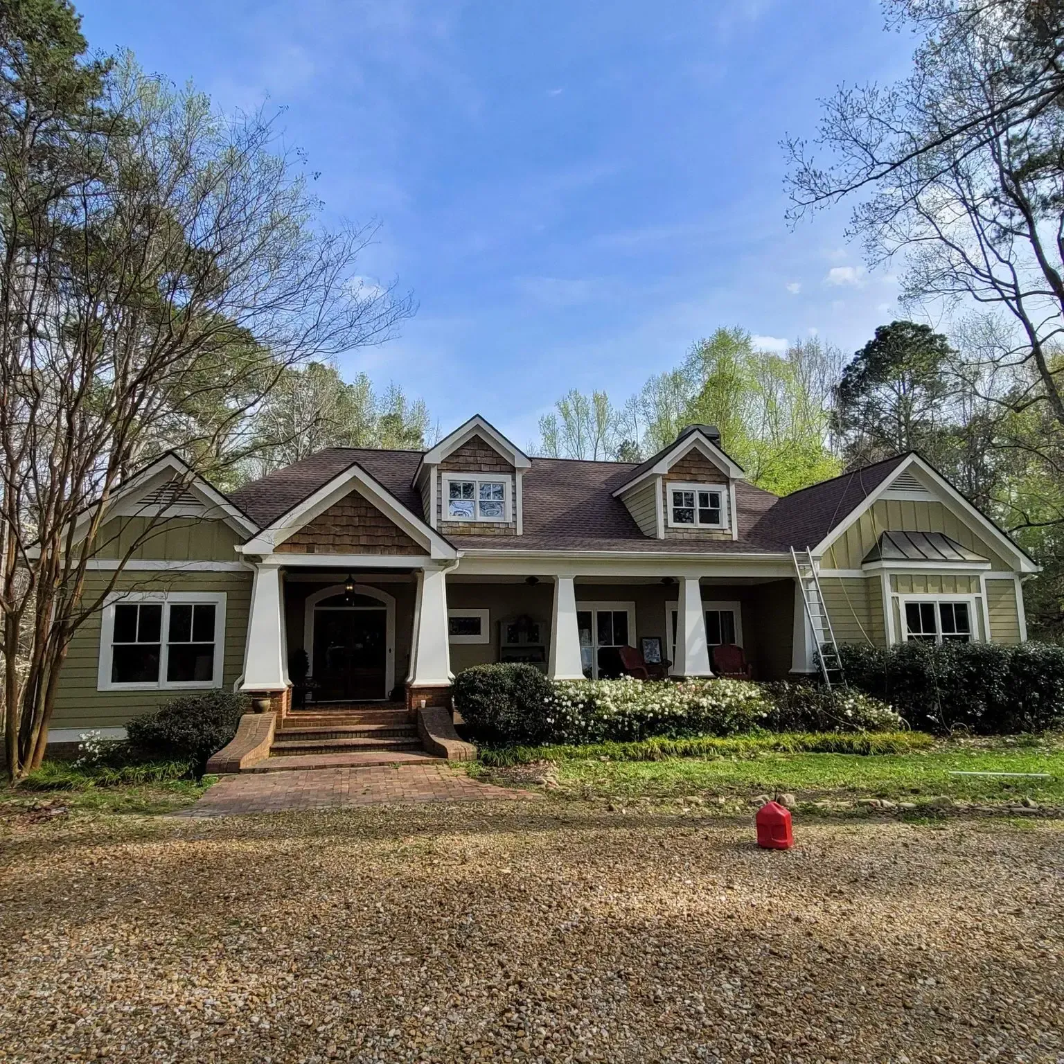 Green house with white trim, brick porch, and a brown roof under a blue sky.