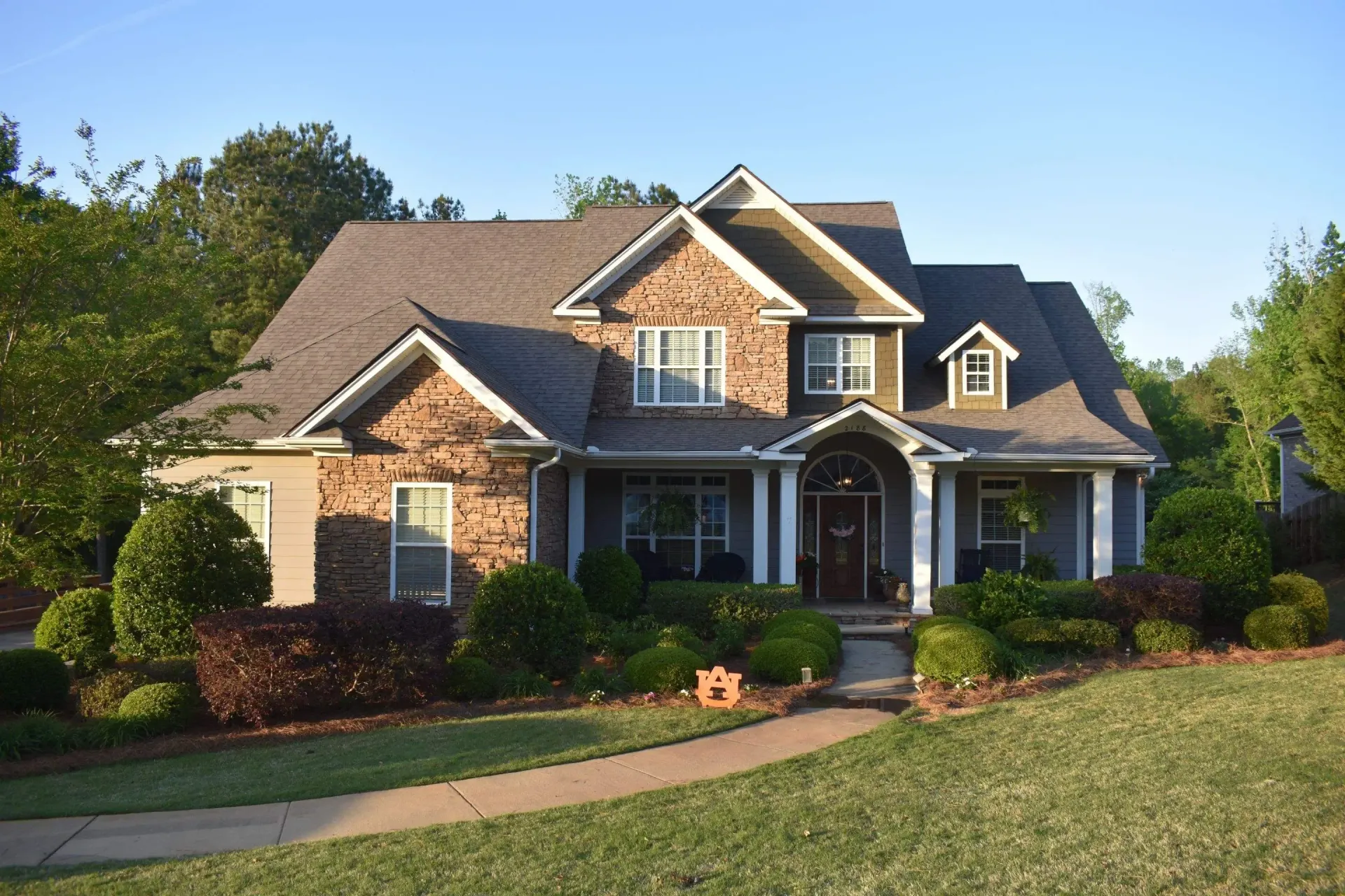 A two-story house with a stone and green facade, set on a grassy lawn with landscaping.