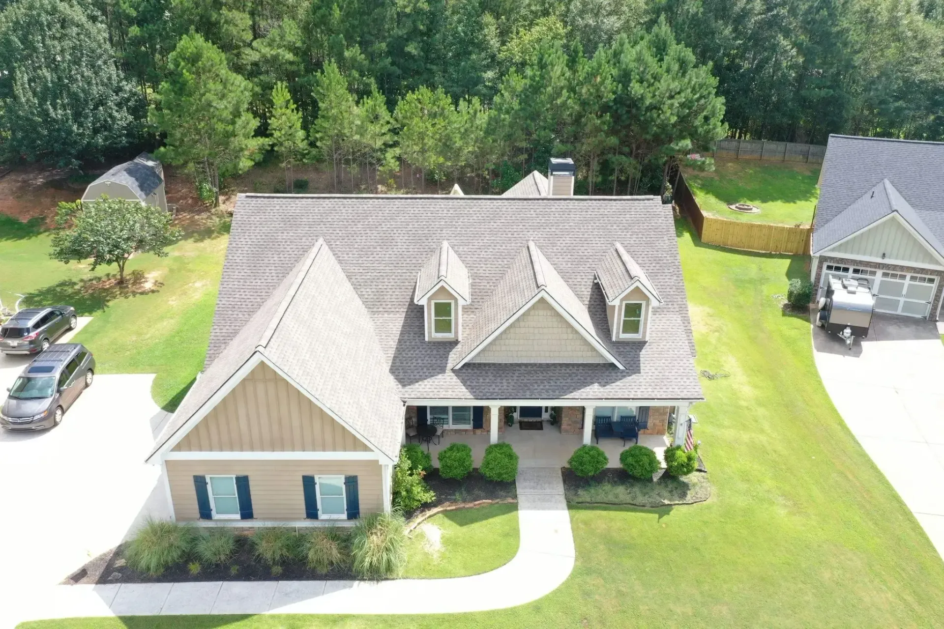 Aerial view of a house with a front porch, lawn, and trees. Two cars parked in front.