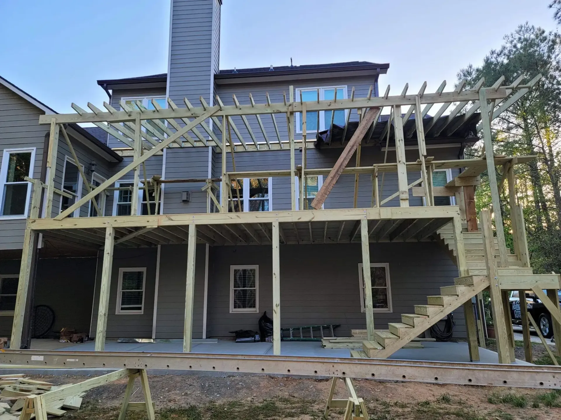 Deck construction in progress; wooden frame attached to a gray house with stairs and pergola.