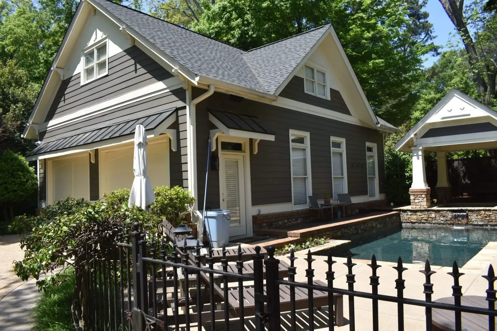 Brown and beige house next to a pool with a black fence.