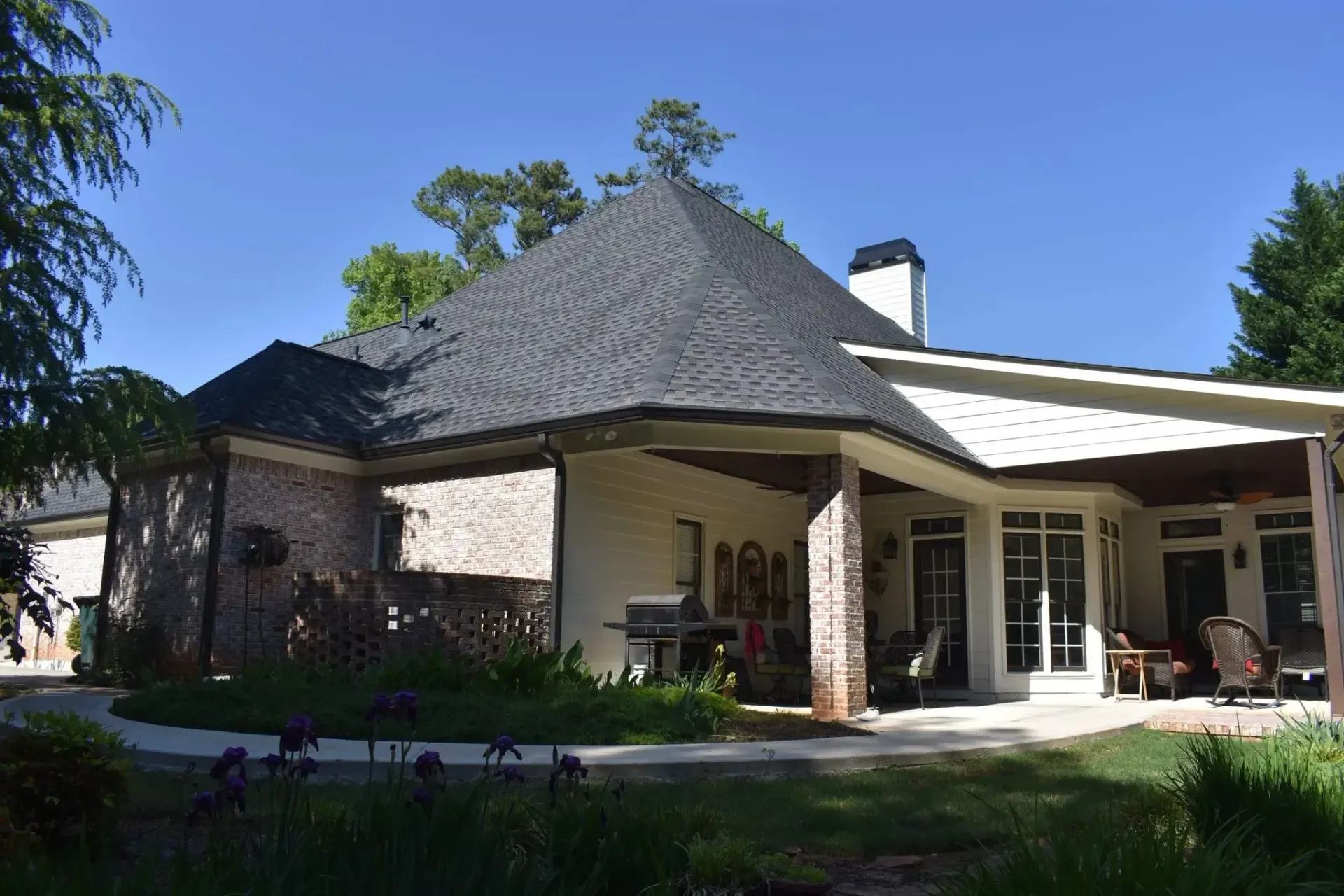 Brick and white stucco house with a dark shingled roof, sunny outdoor patio and garden.