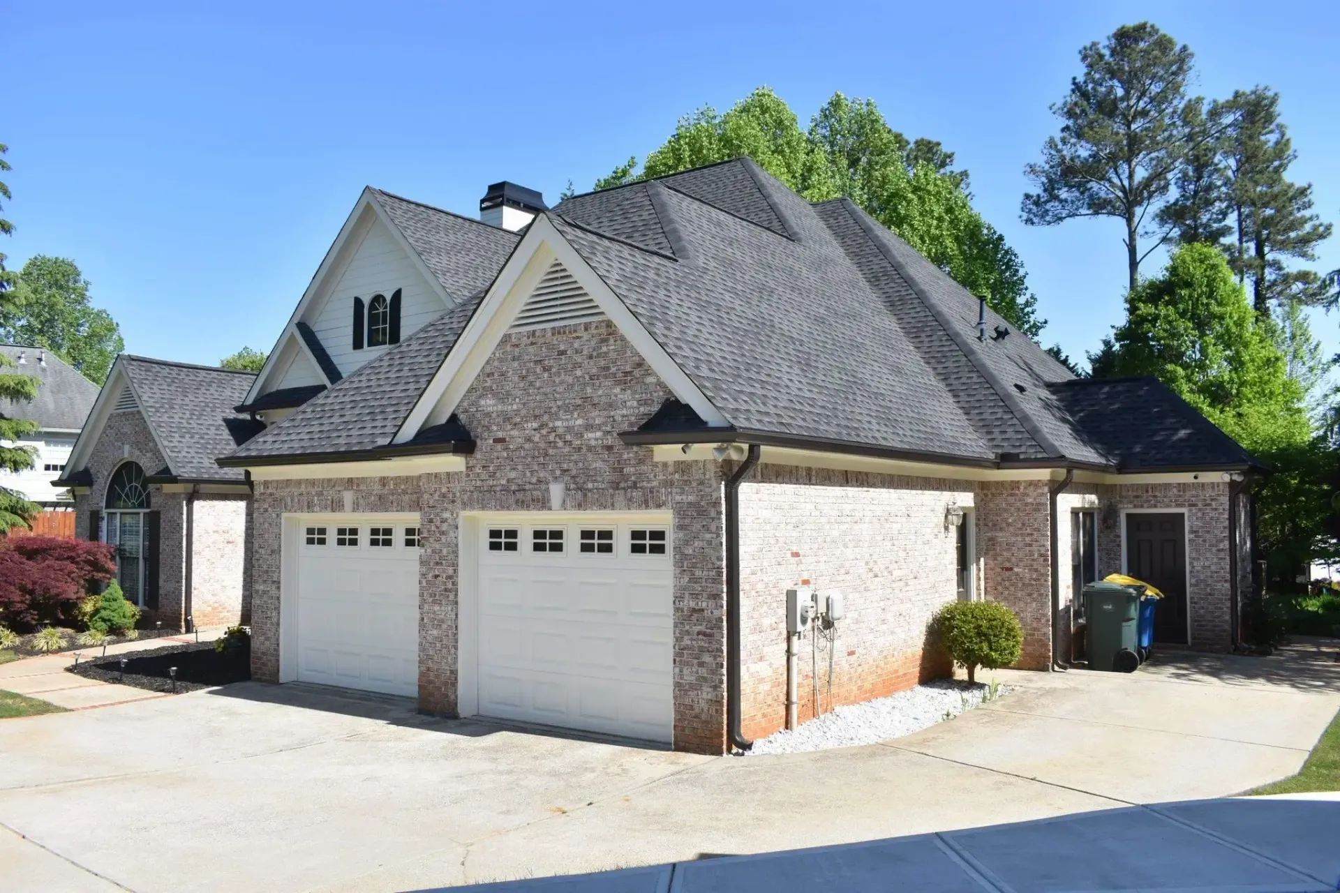 Brick house with a two-car garage and black roof against a clear, blue sky.