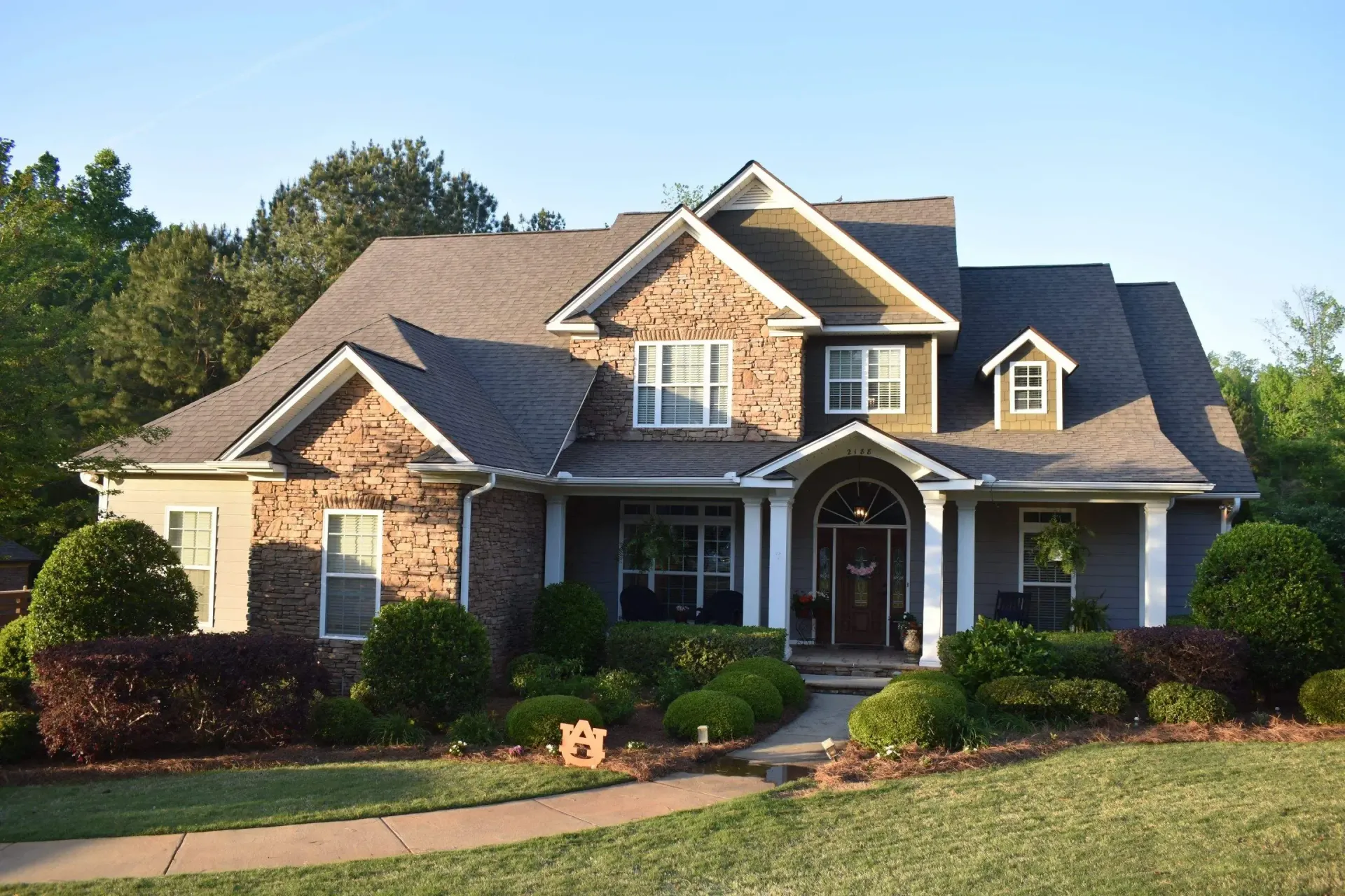Two-story brick and siding house with green lawn and landscaping.