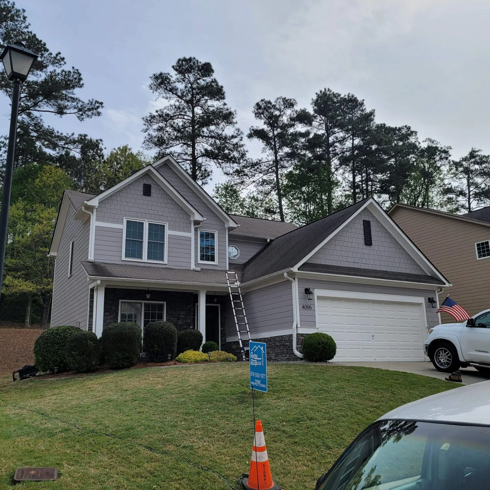 Two-story gray house with white garage door and a truck parked in front. Trees and grass surround.