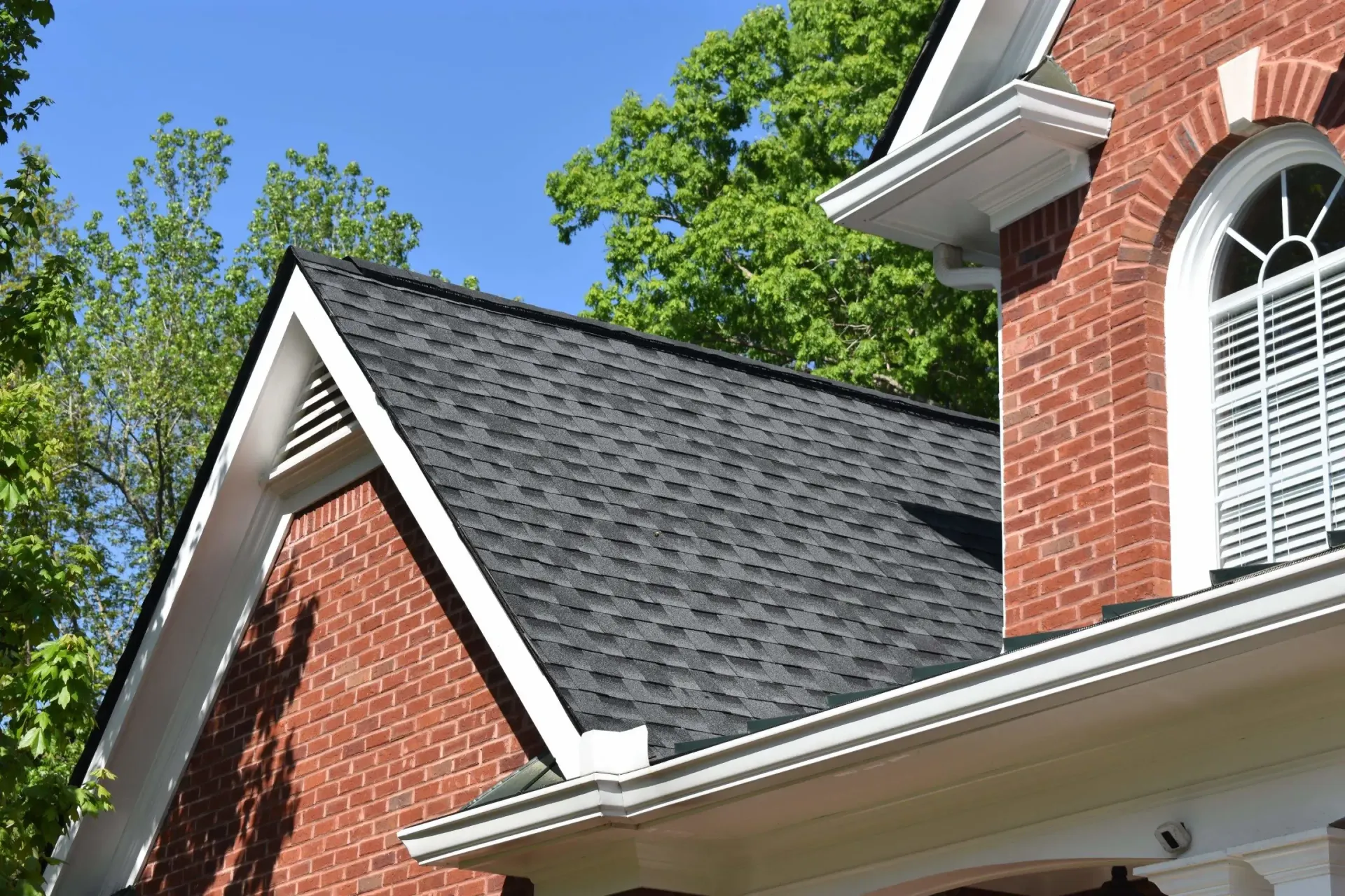Brick house with black shingled roof and white trim, under a bright blue sky.