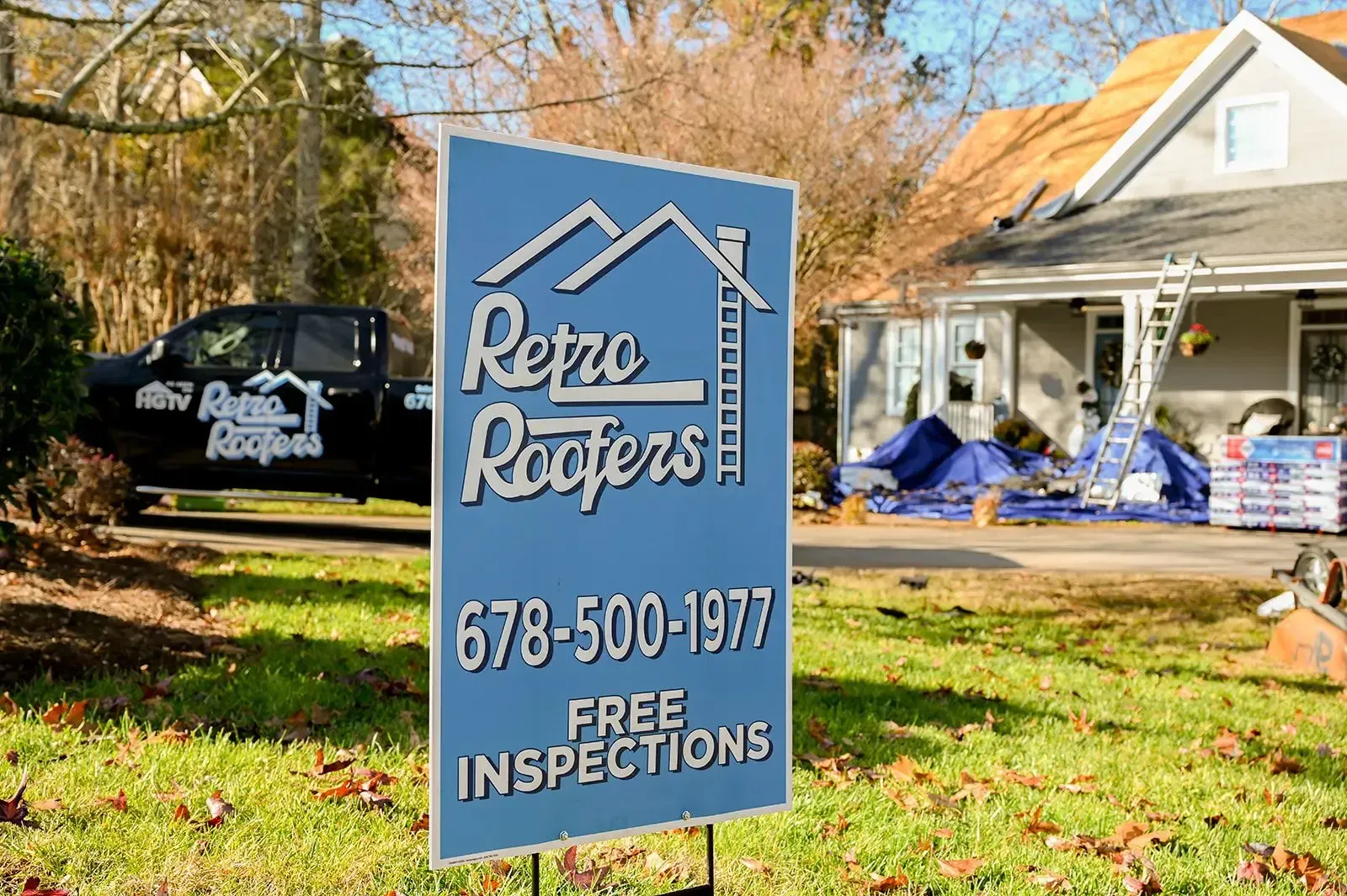 Sign for Retro Roofers in front of a house being worked on, black truck, blue sign, phone number.