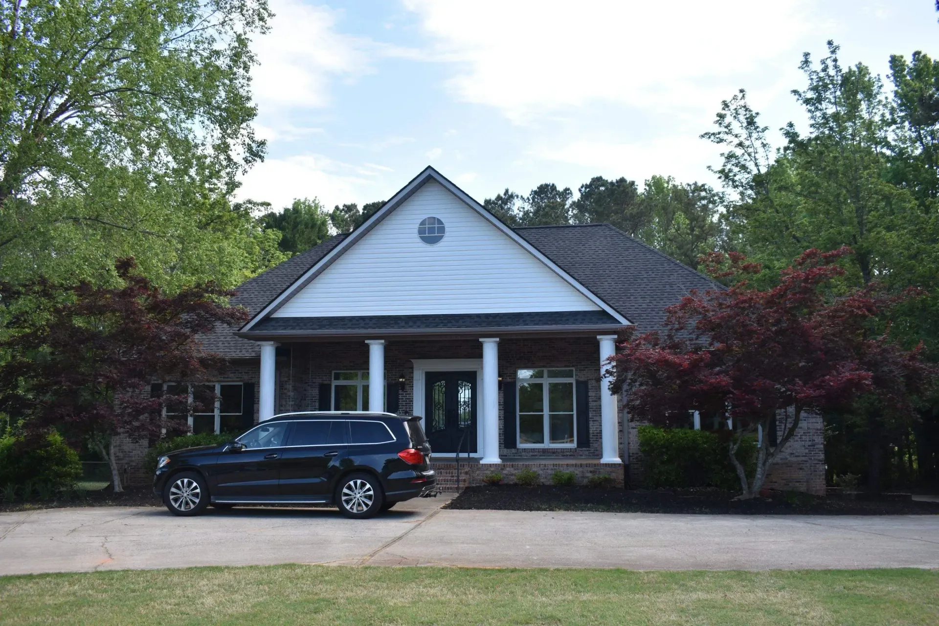 Black SUV parked in front of a house with white columns and a blue door. Trees surround the house.