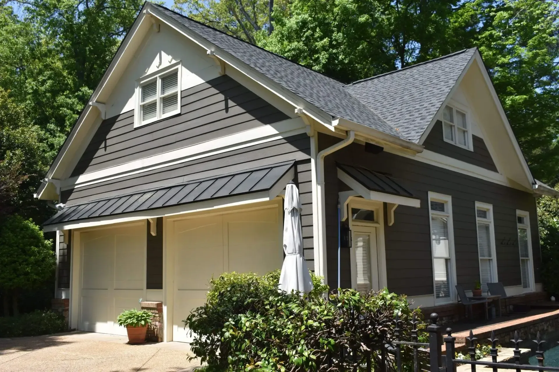 Brown and white two-story building with dark roof and trim; garage, windows, and greenery.