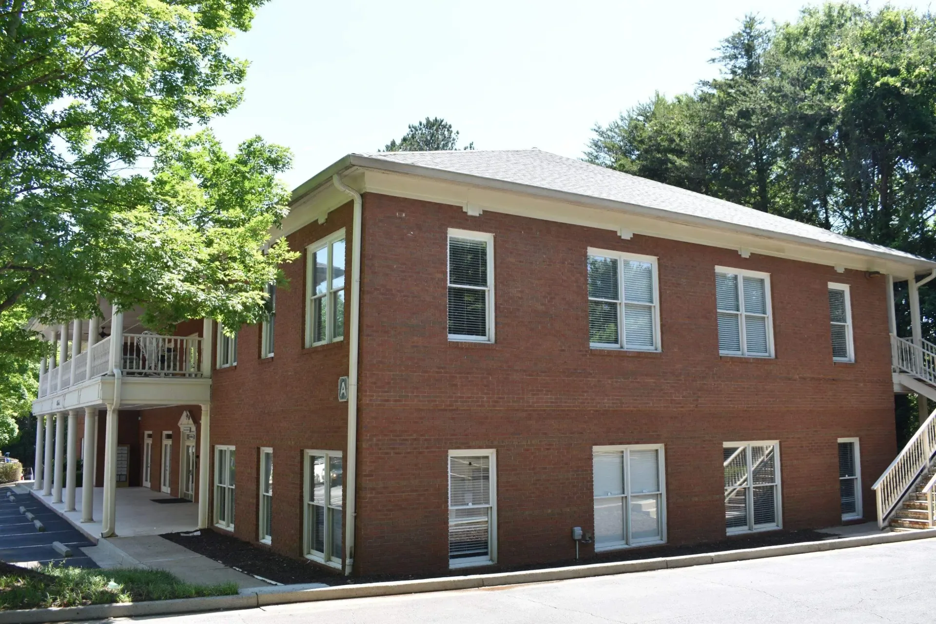 Two-story brick building with white trim and porch. Trees frame the structure.
