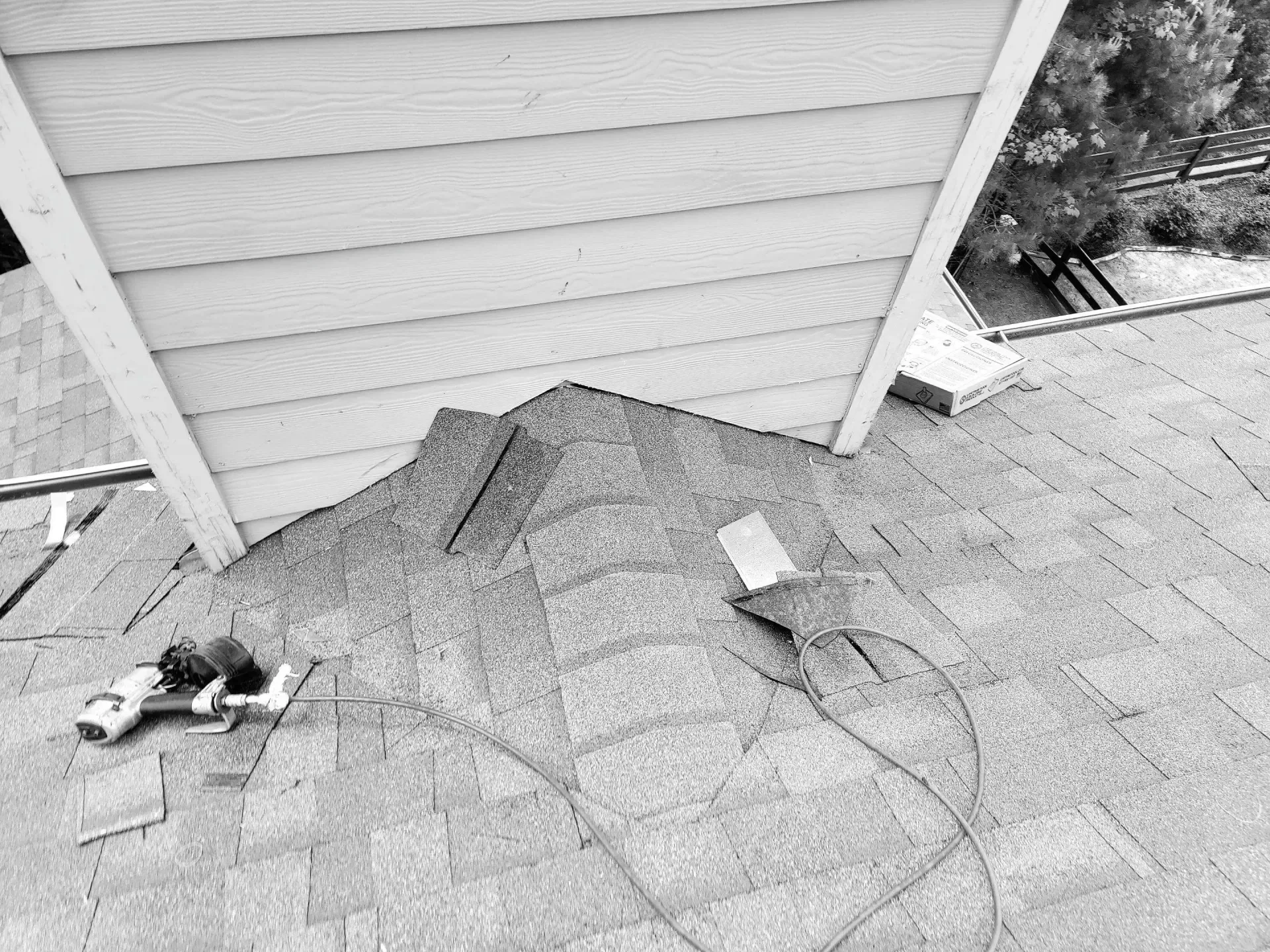 Overhead shot of a roof with shingles, tools, and part of a building’s siding.