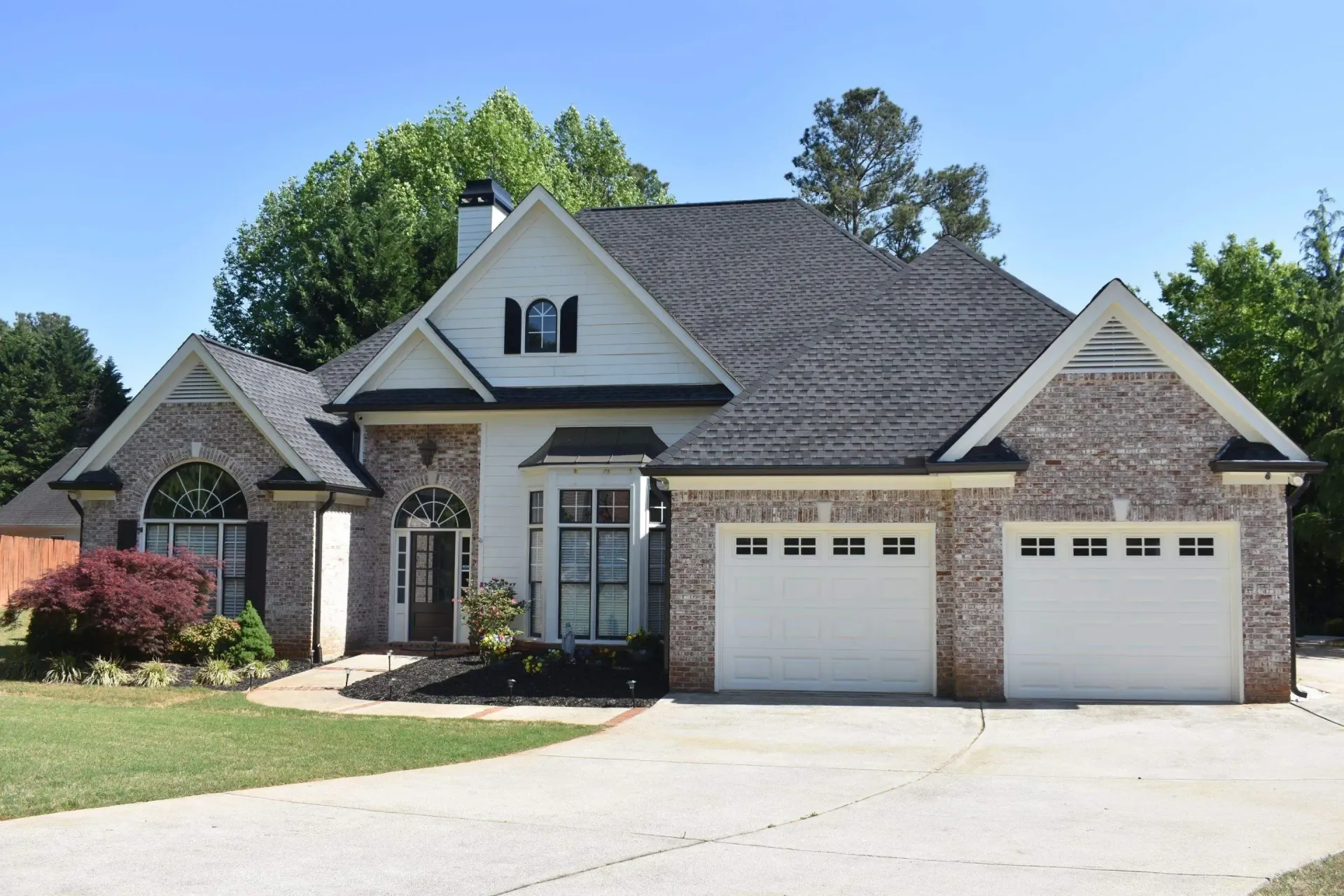A brick house with white trim, two-car garage, and a dark roof under a blue sky.