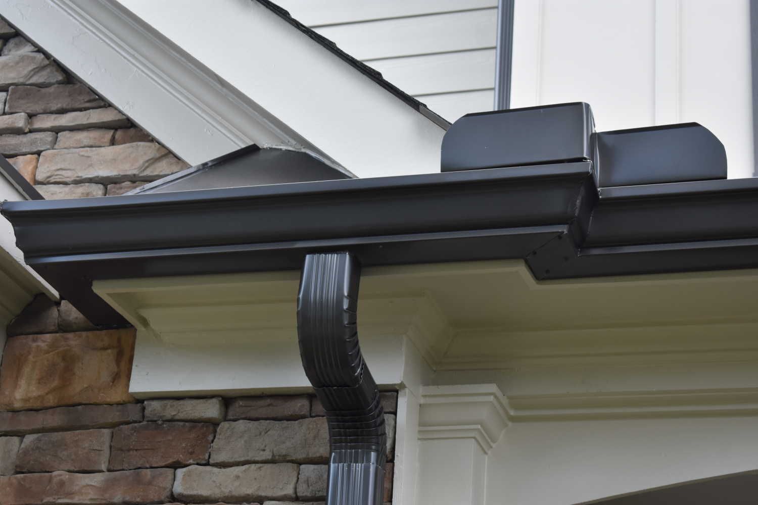 Dark brown rain gutters on a white trim house with stone accents.