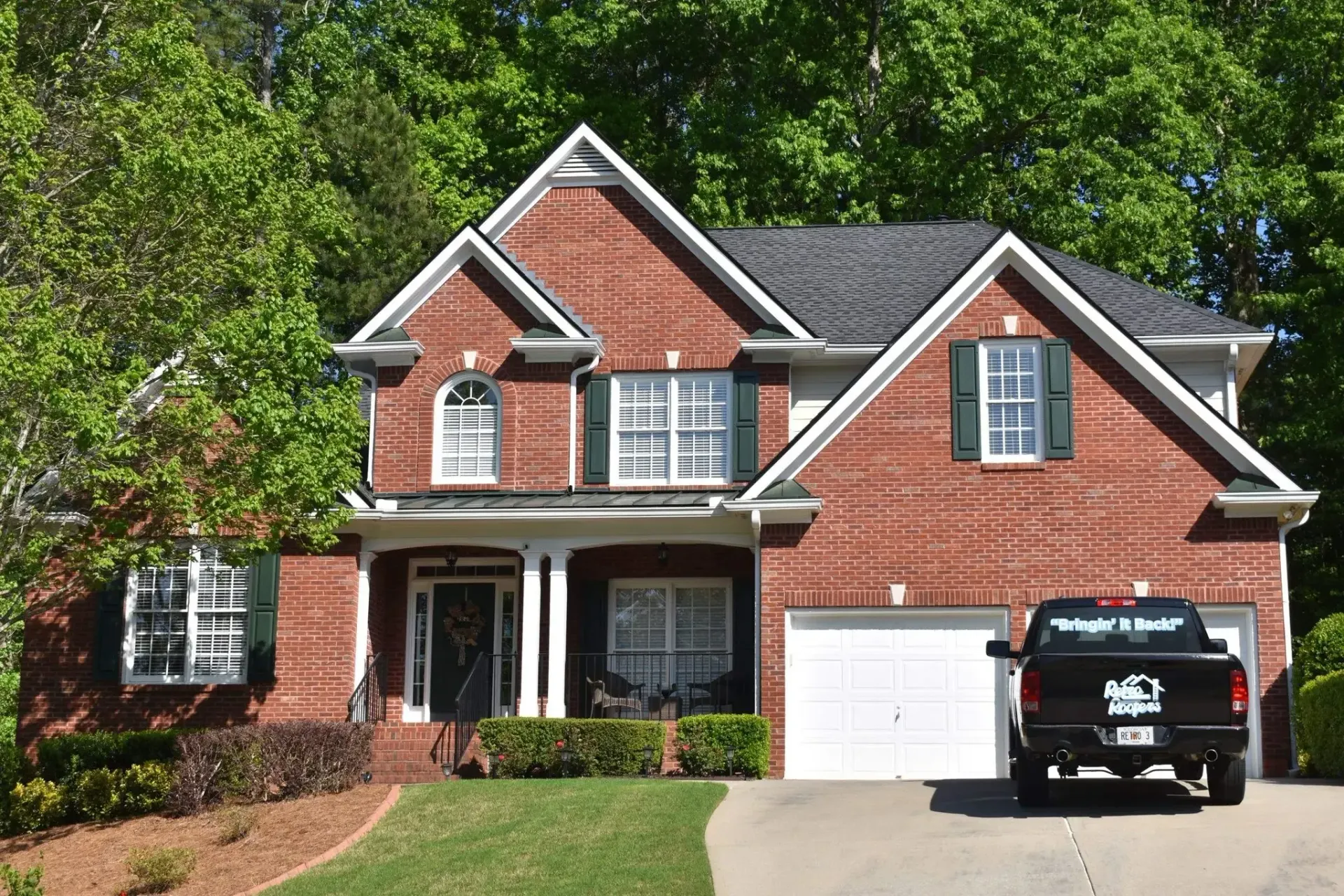 Red brick house with a black truck parked in the driveway. Green shutters and landscaping.