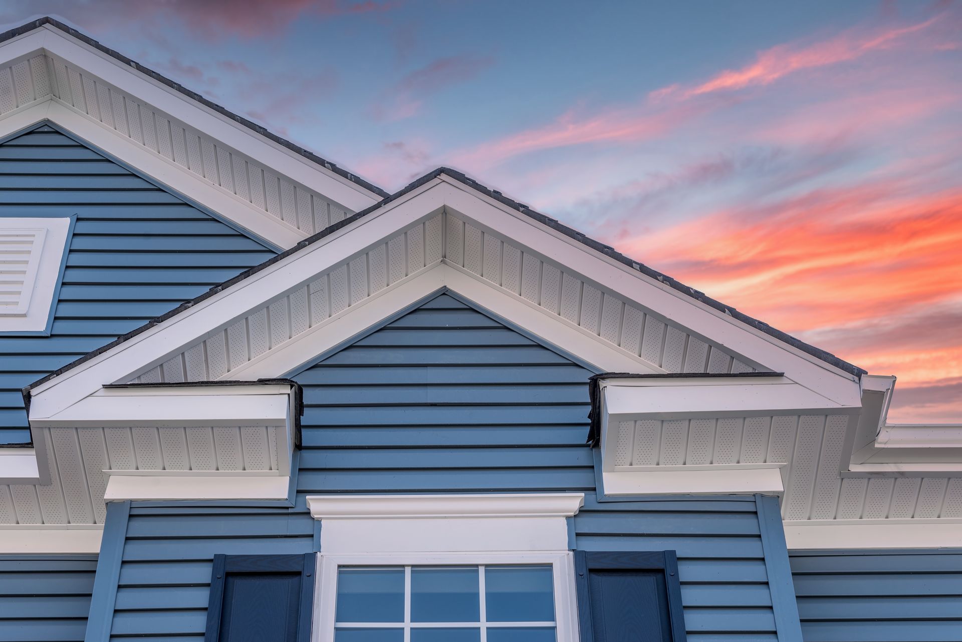 Blue house exterior with white trim against a sunset sky.