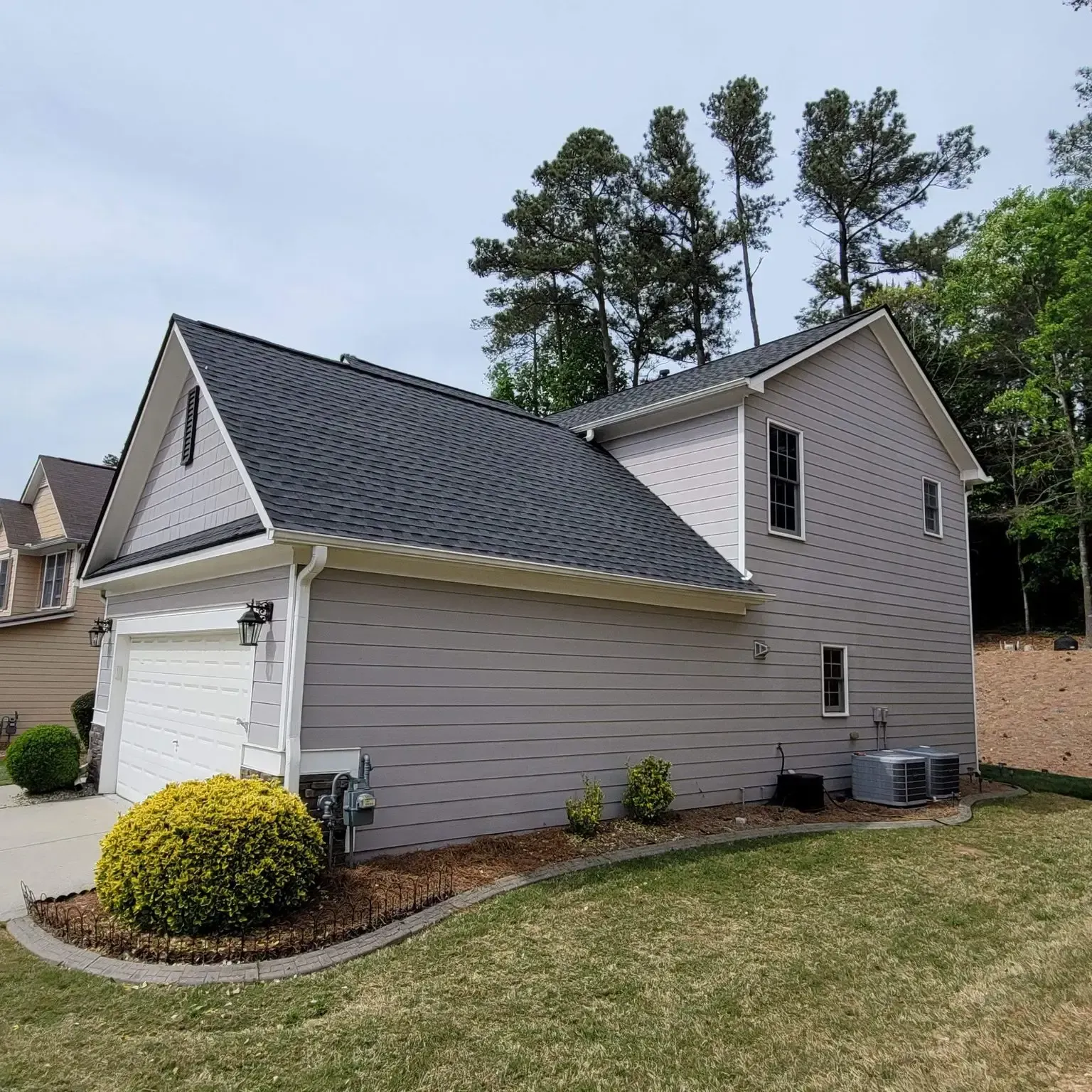 Two-story house with gray siding, dark roof, garage, and landscaping.