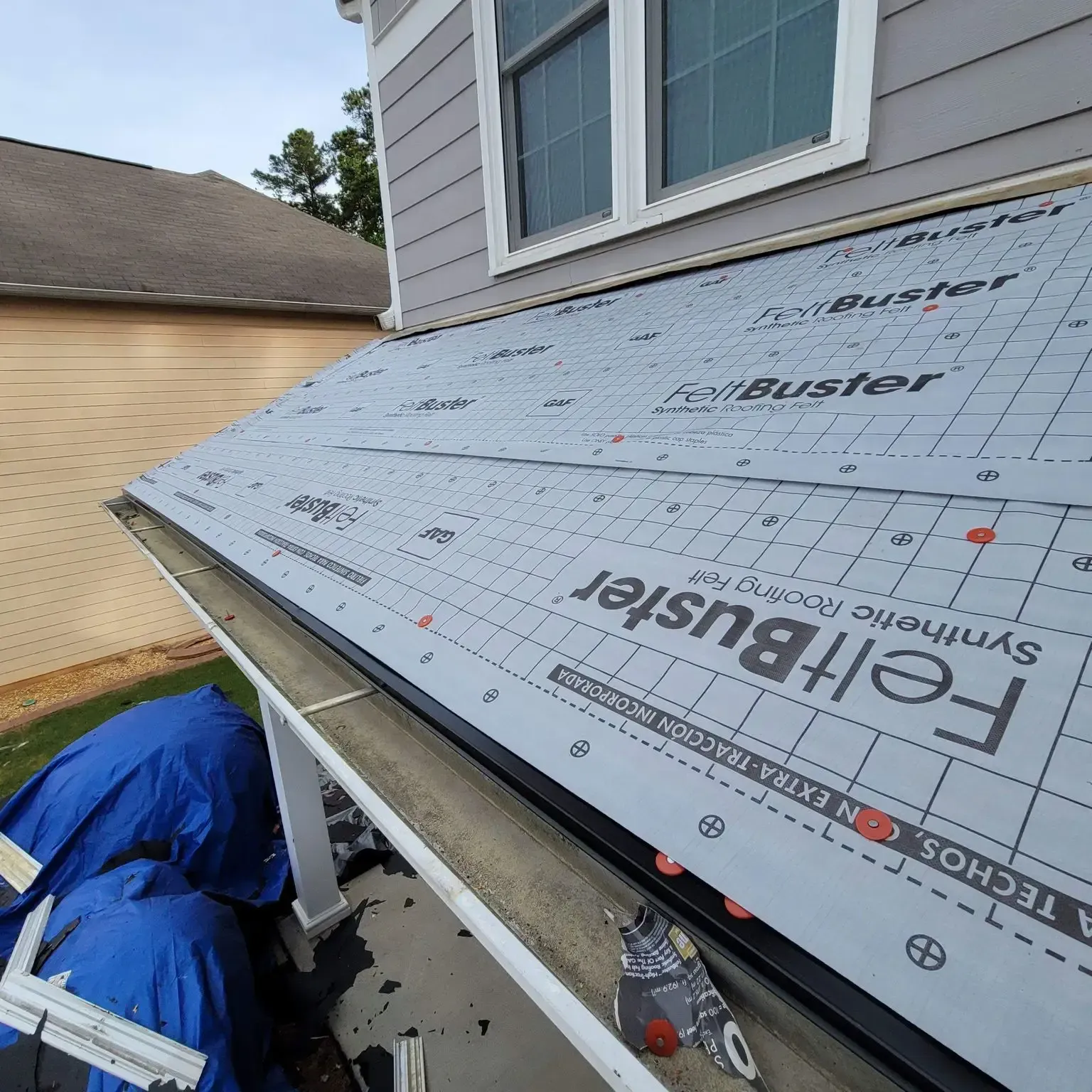 Roofer installing synthetic felt underlayment on a house roof, with a gutter in the foreground.