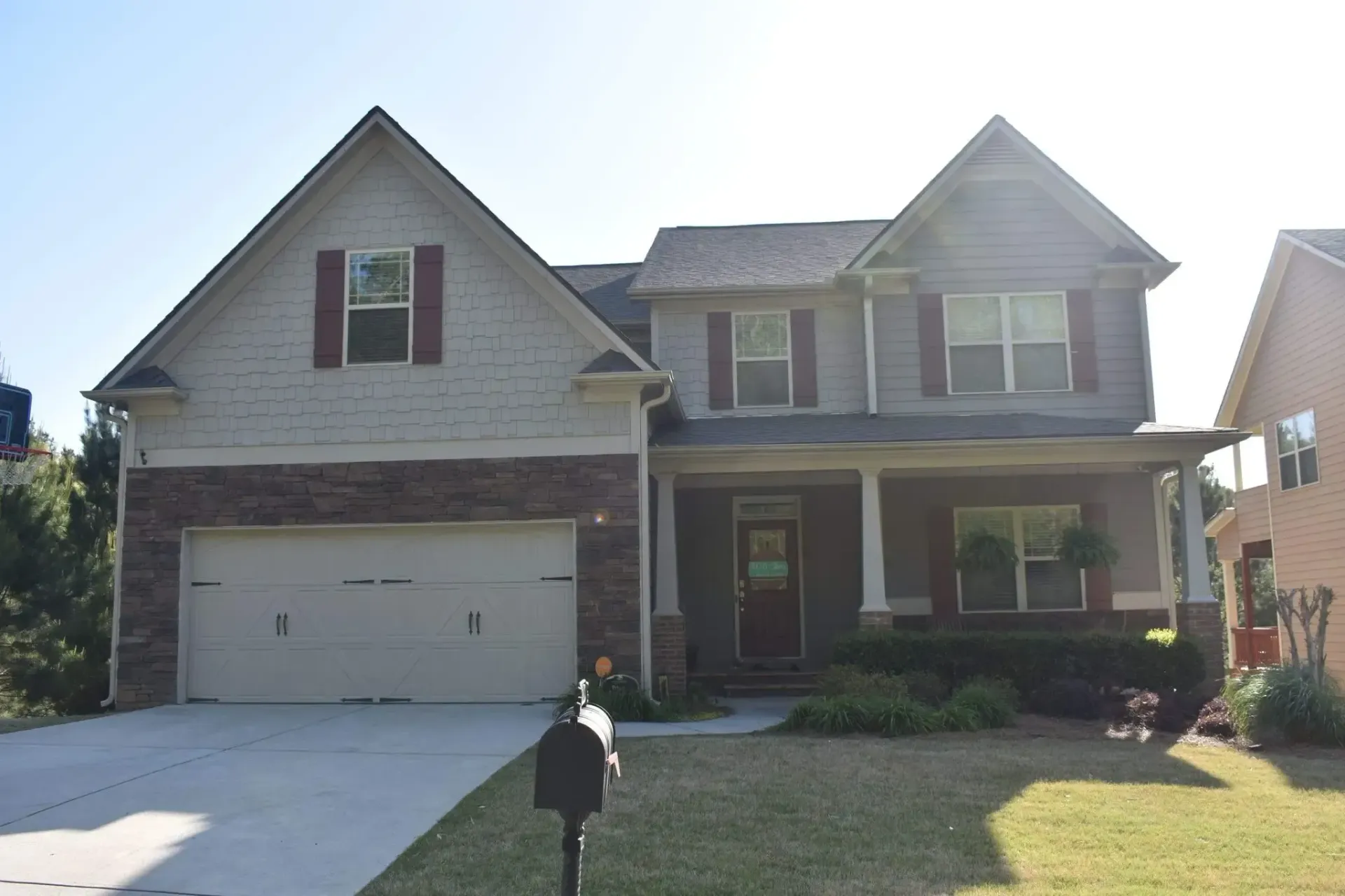 Two-story gray house with a porch, garage, and brick facade; blue sky in the background.