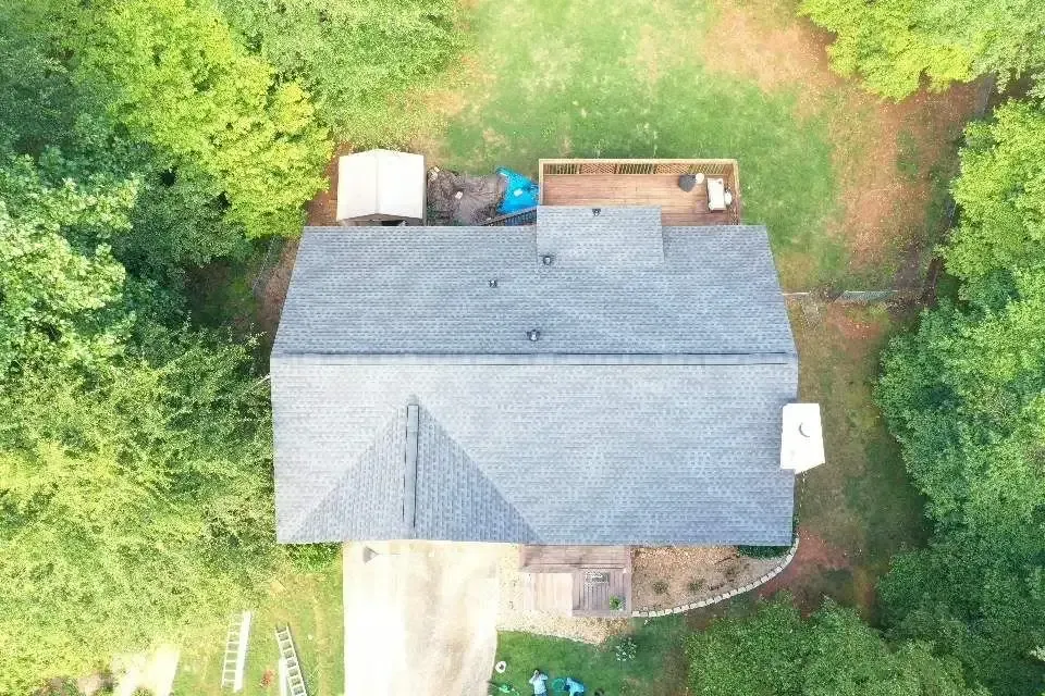 Overhead view of a house with gray roof, surrounded by green trees and grass.