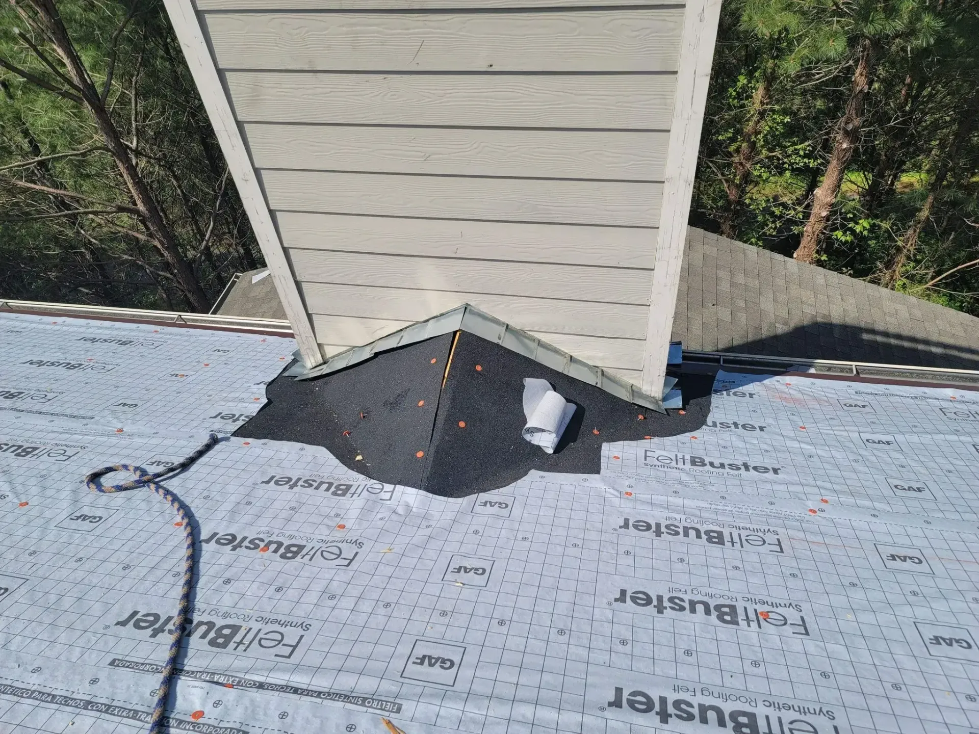 Roof with chimney and black flashing, trees in the background.
