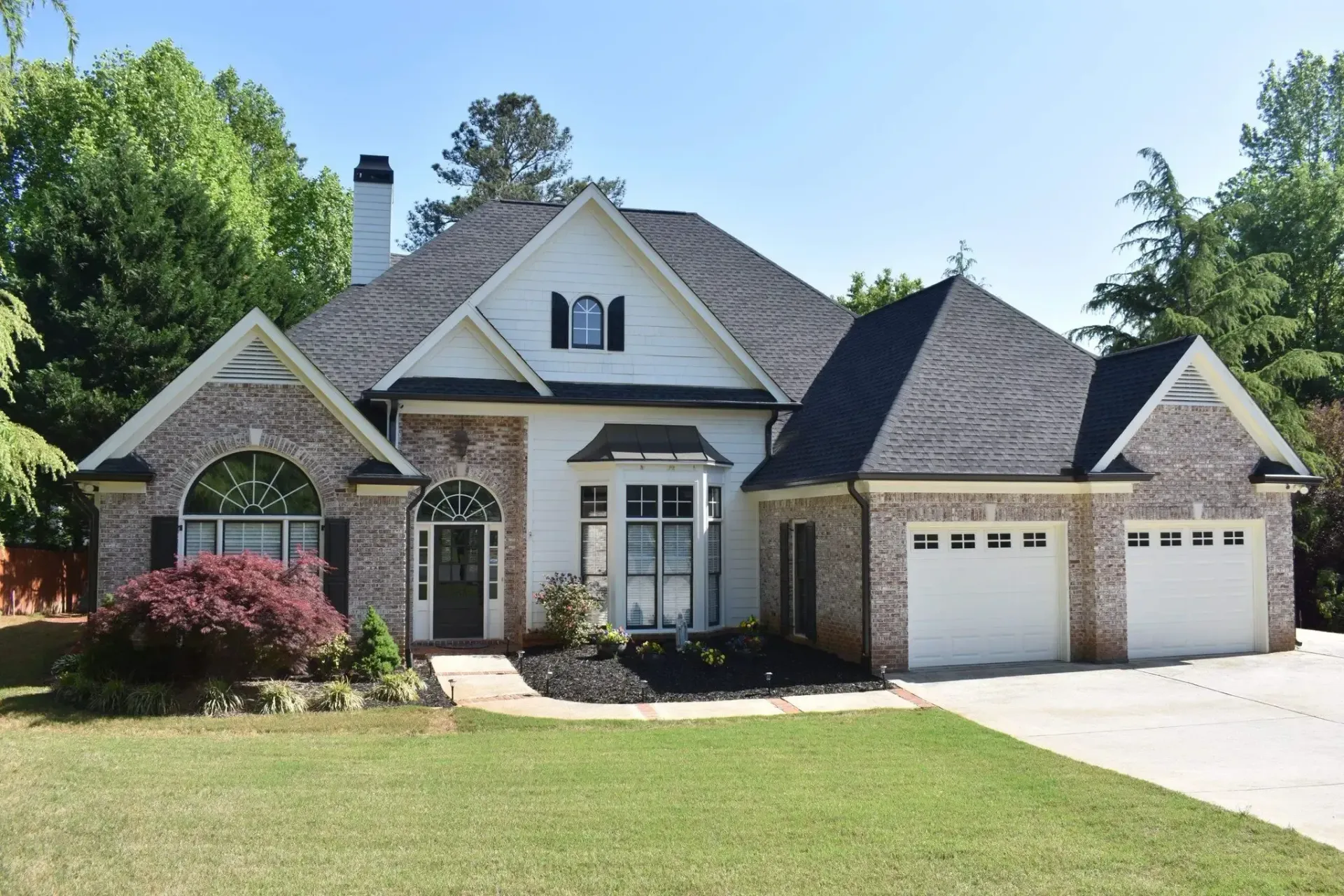 Suburban house with brick accents, white walls, and two-car garage on a green lawn.