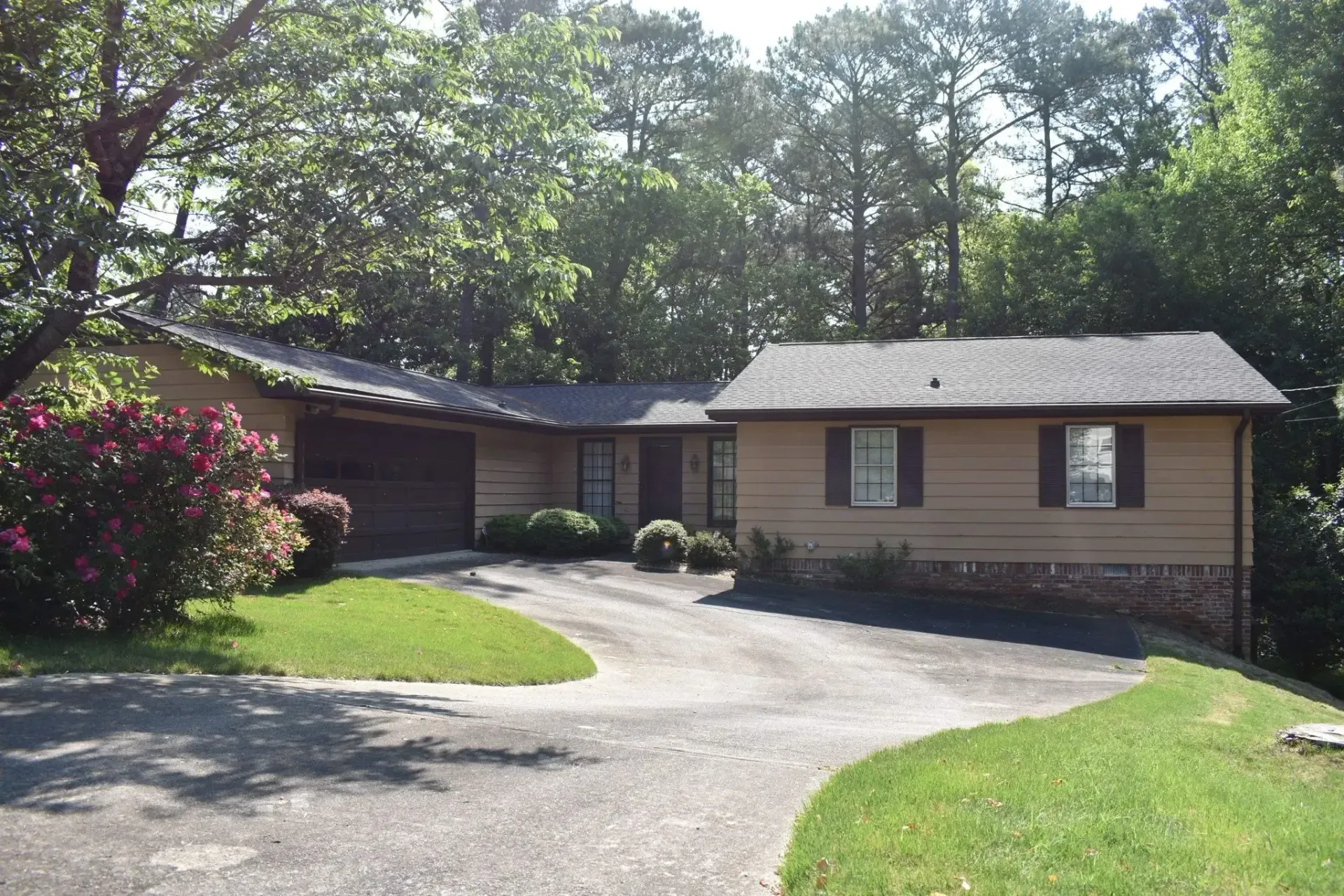 Beige ranch home with brown trim, driveway, and surrounding trees.