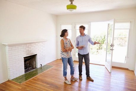 A man and a woman are standing in an empty living room.